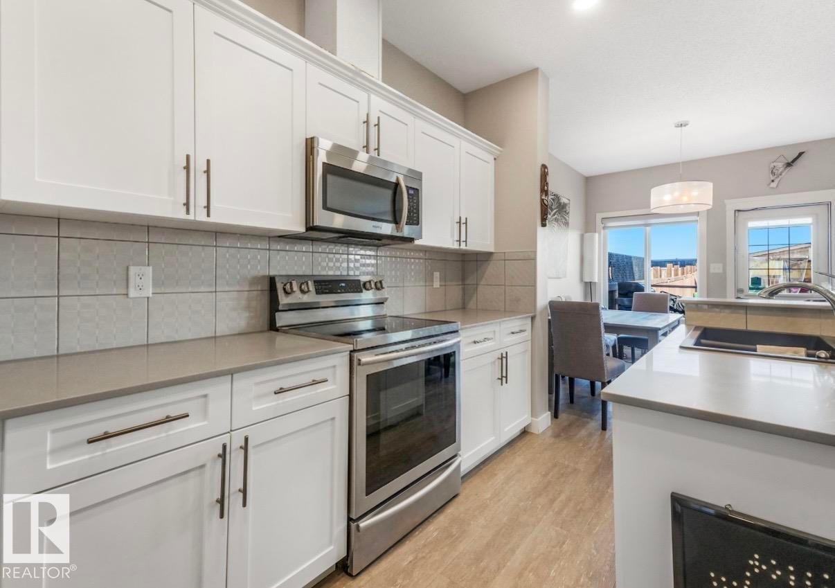 Modern kitchen featuring white shaker cabinetry, stainless steel appliances, light gray countertops, and a patterned tile backsplash - 17171 38 Street, Edmonton, AB