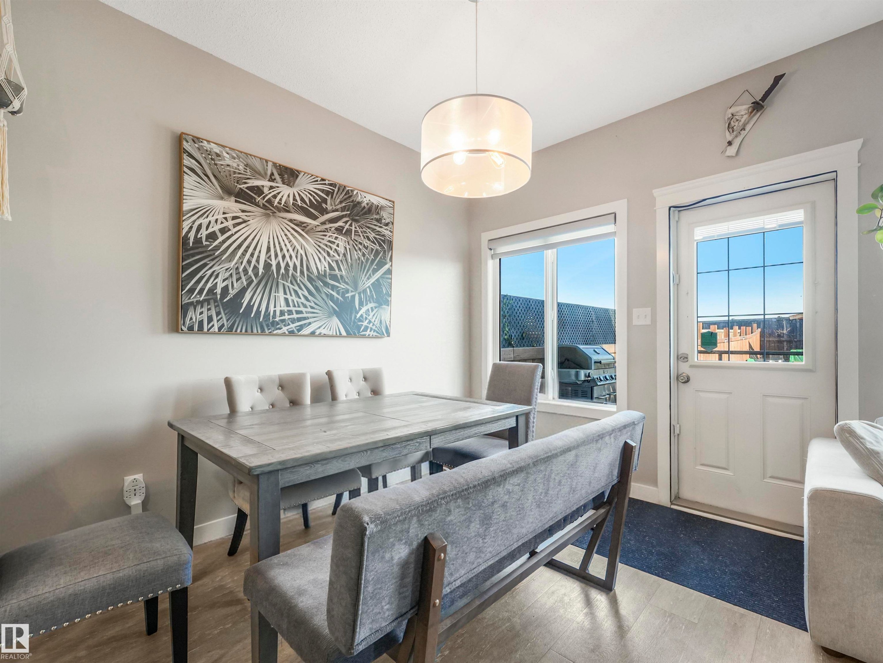 Bright dining area featuring wood-finish flooring, a contemporary drum pendant light fixture, and a white paneled door with grid-patterned glass - 17171 38 Street, Edmonton, AB