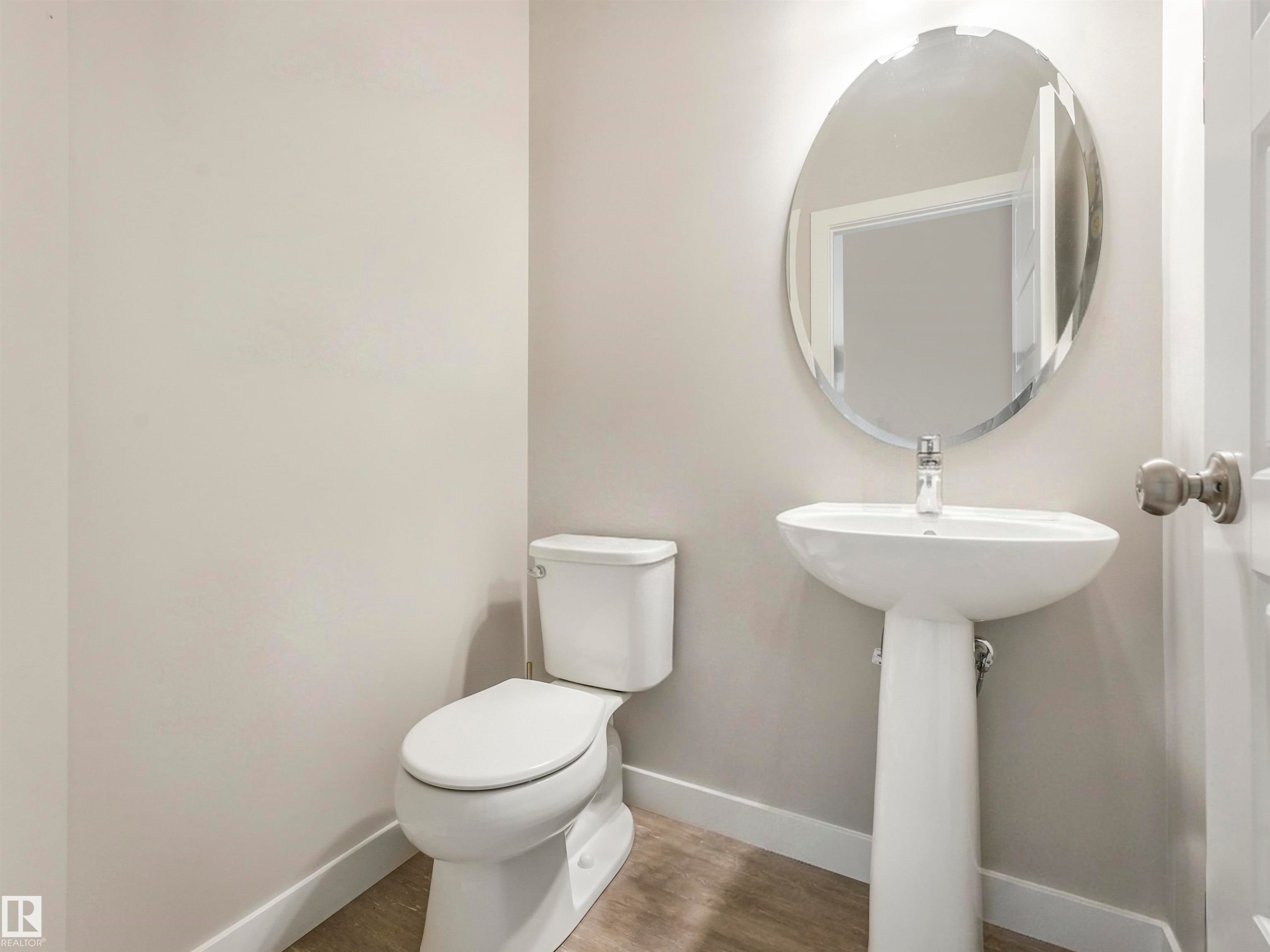 Bathroom featuring a white pedestal sink with a chrome faucet, a matching toilet, and an oval wall mirror - 17171 38 Street, Edmonton, AB