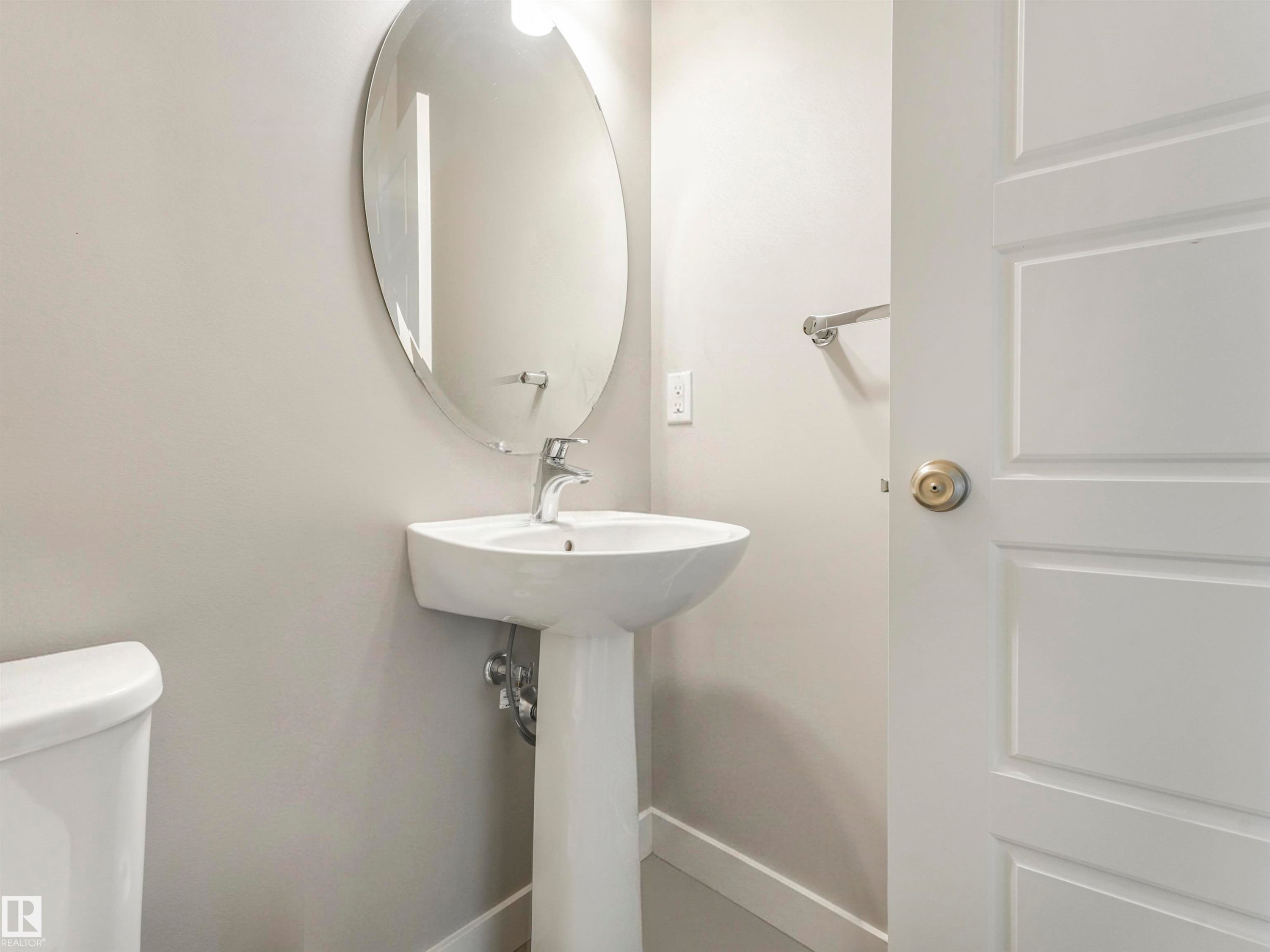 Pedestal sink with chrome faucet, complemented by an oval wall-mounted mirror - 17171 38 Street, Edmonton, AB