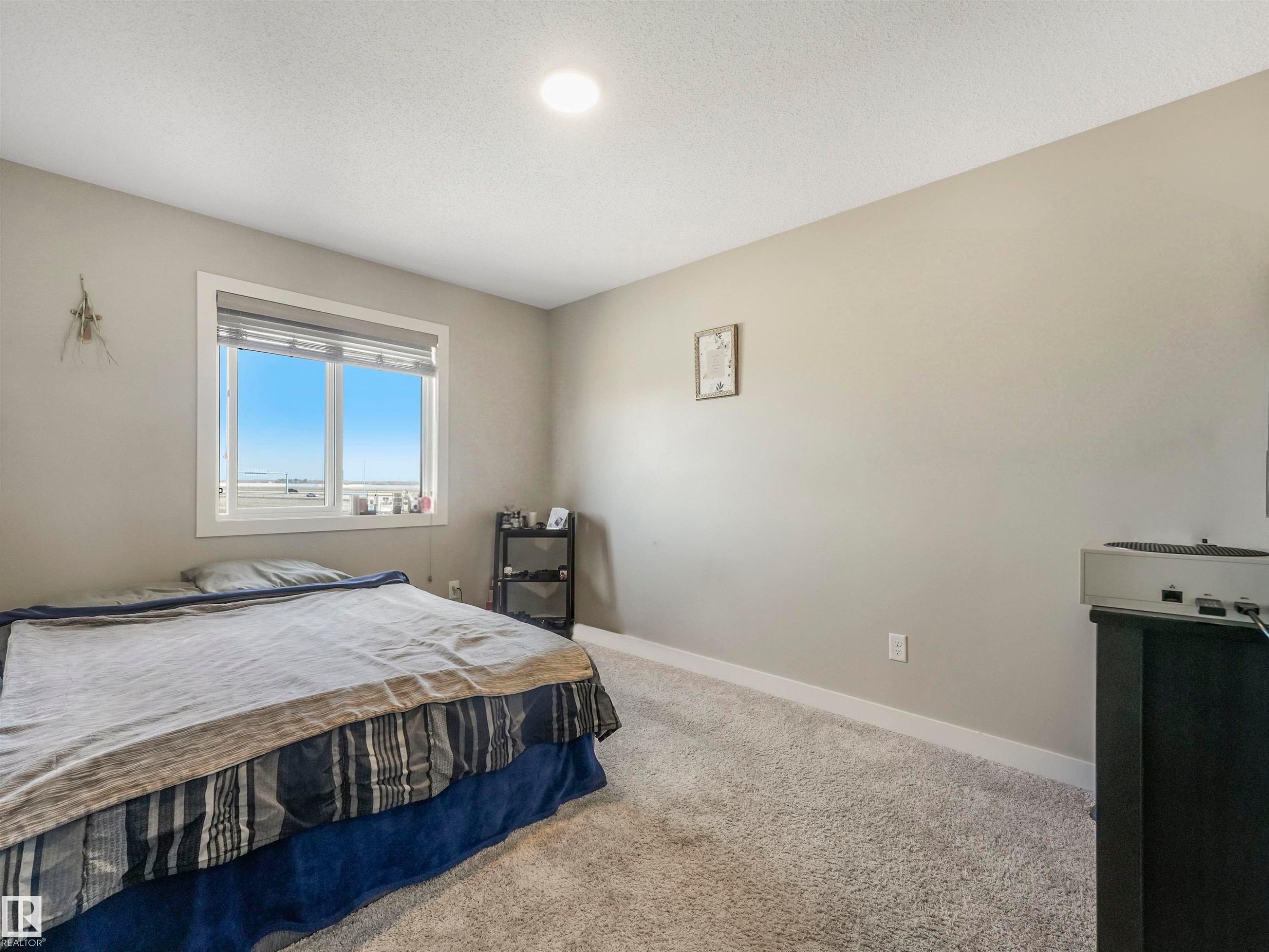 Bright room featuring a window with horizontal blinds, neutral wall paint, and light-toned carpet flooring - 17171 38 Street, Edmonton, AB