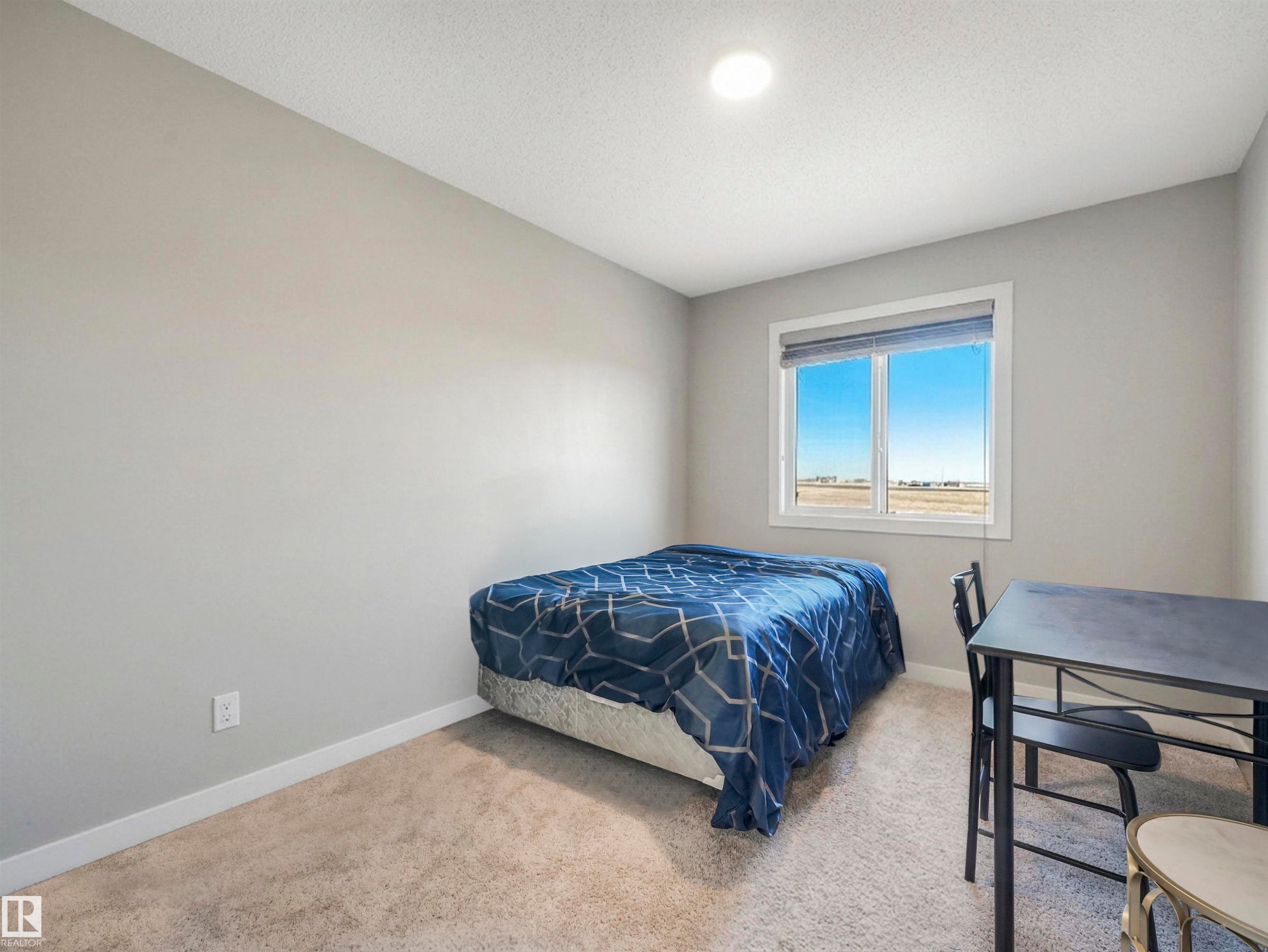 Carpeted bedroom featuring a large window, neutral wall paint, and white baseboards - 17171 38 Street, Edmonton, AB
