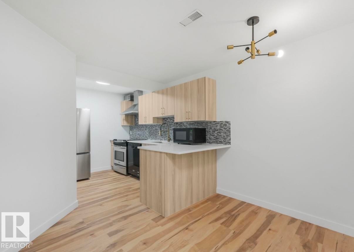 Modern kitchen featuring light wood-finish cabinetry, stainless steel appliances, a mosaic tile backsplash, and light-toned countertops - 17171 38 Street, Edmonton, AB