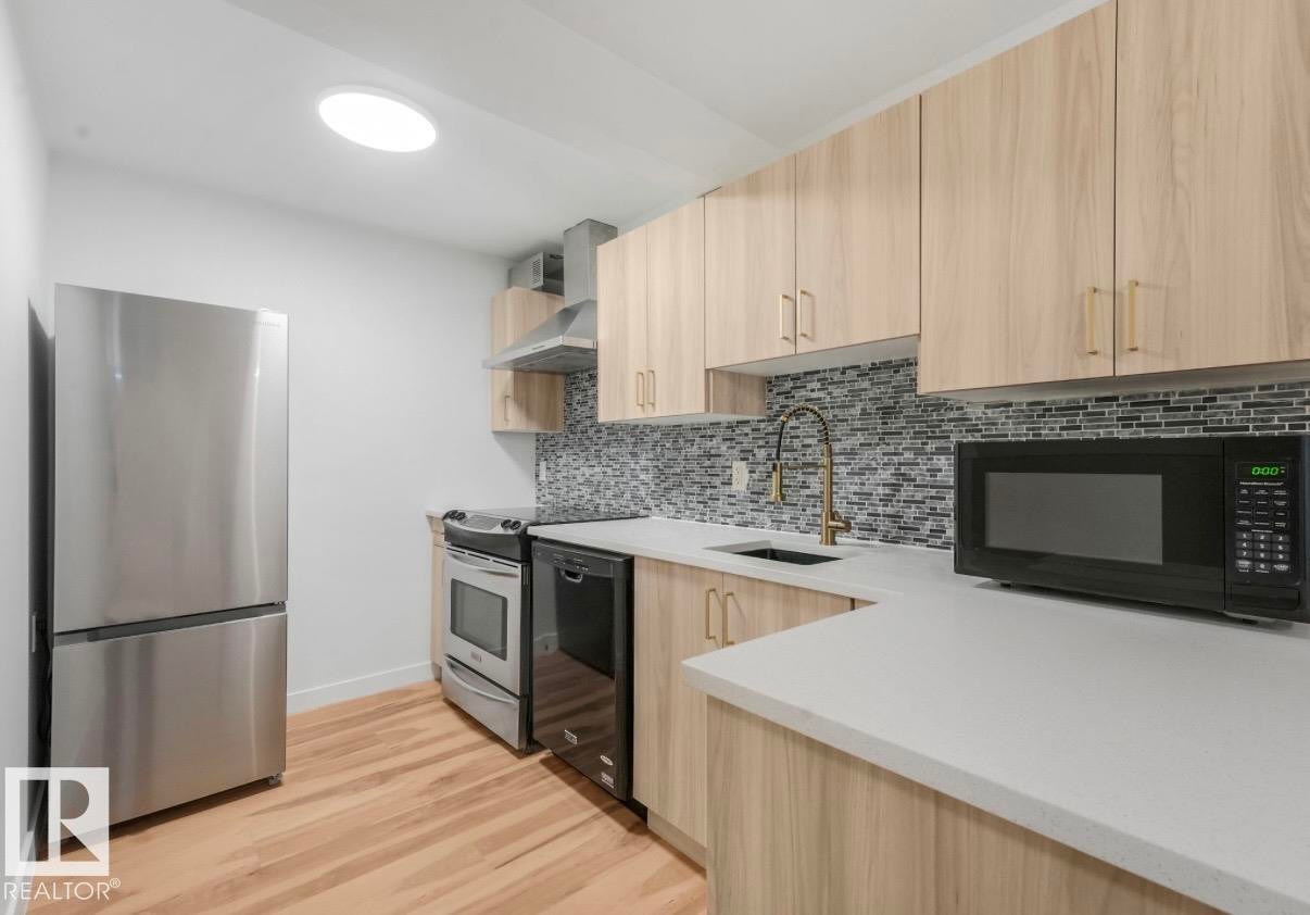 Kitchen featuring light wood-finish cabinetry, light countertops, mosaic tile backsplash, and stainless steel appliances - 17171 38 Street, Edmonton, AB