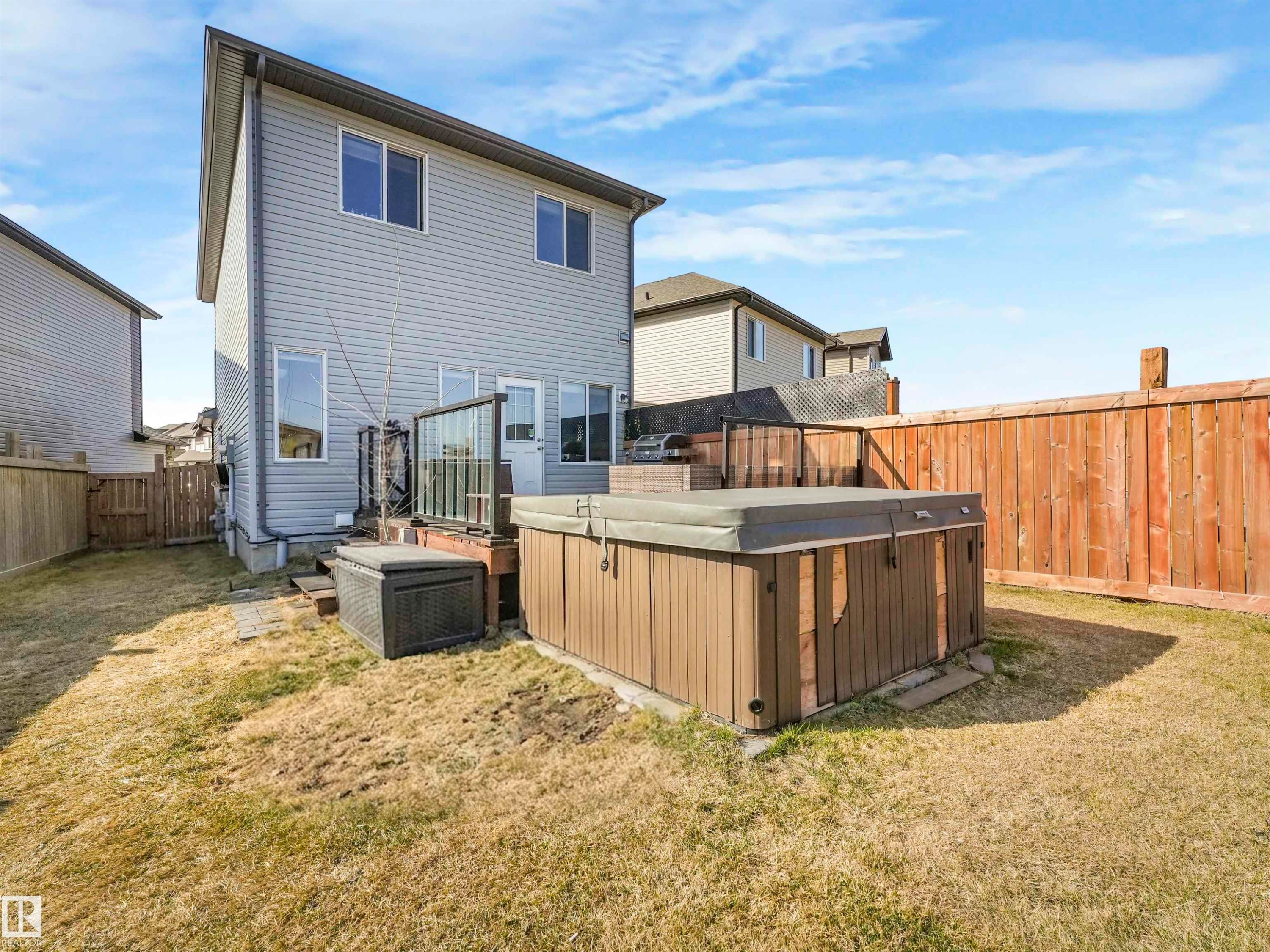 Private backyard featuring a hot tub, wood privacy fence, and a raised composite deck with glass railings - 17171 38 Street, Edmonton, AB