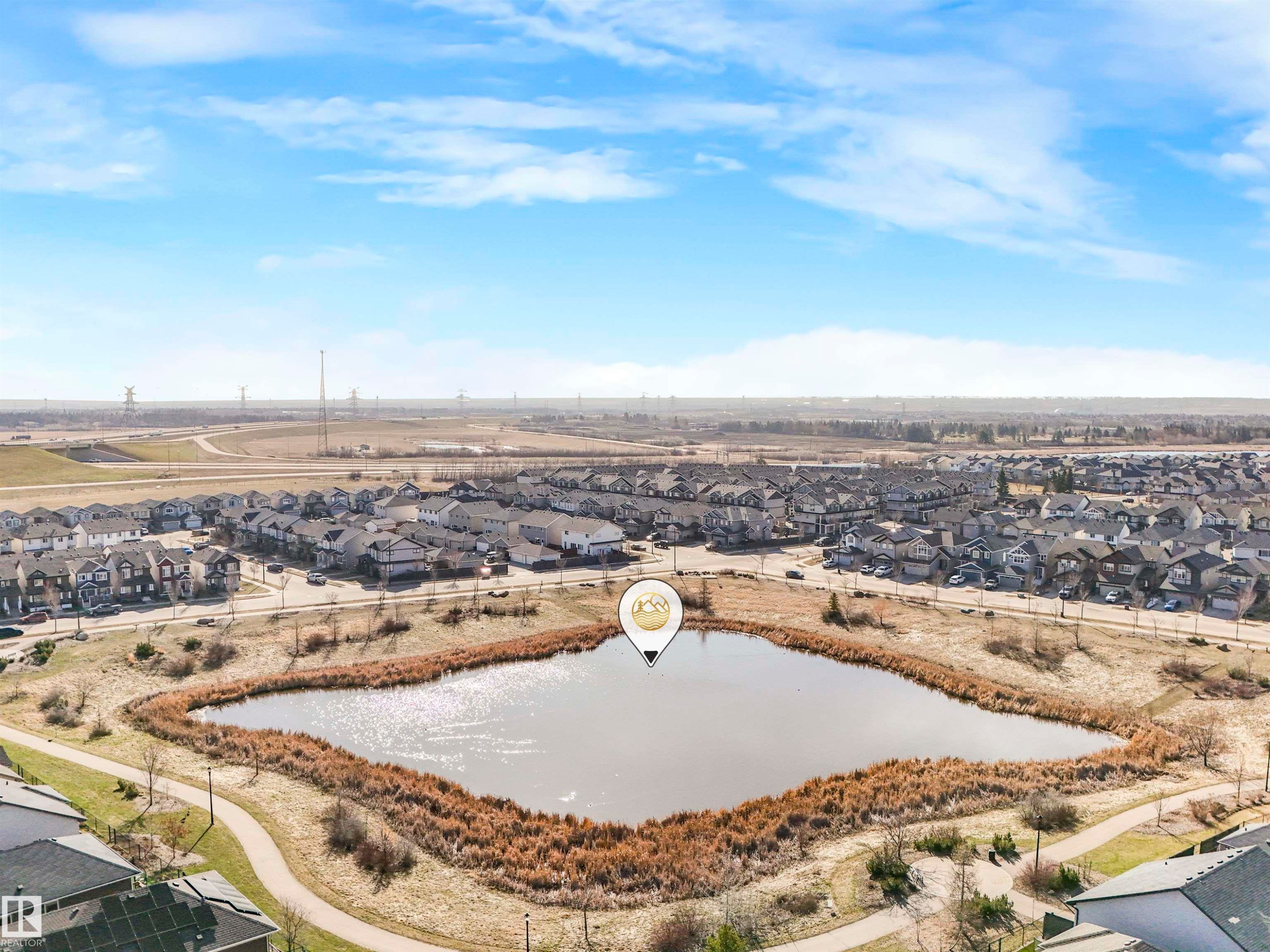 Community setting featuring a central pond with natural reed landscaping, surrounded by a paved walking path - 17171 38 Street, Edmonton, AB
