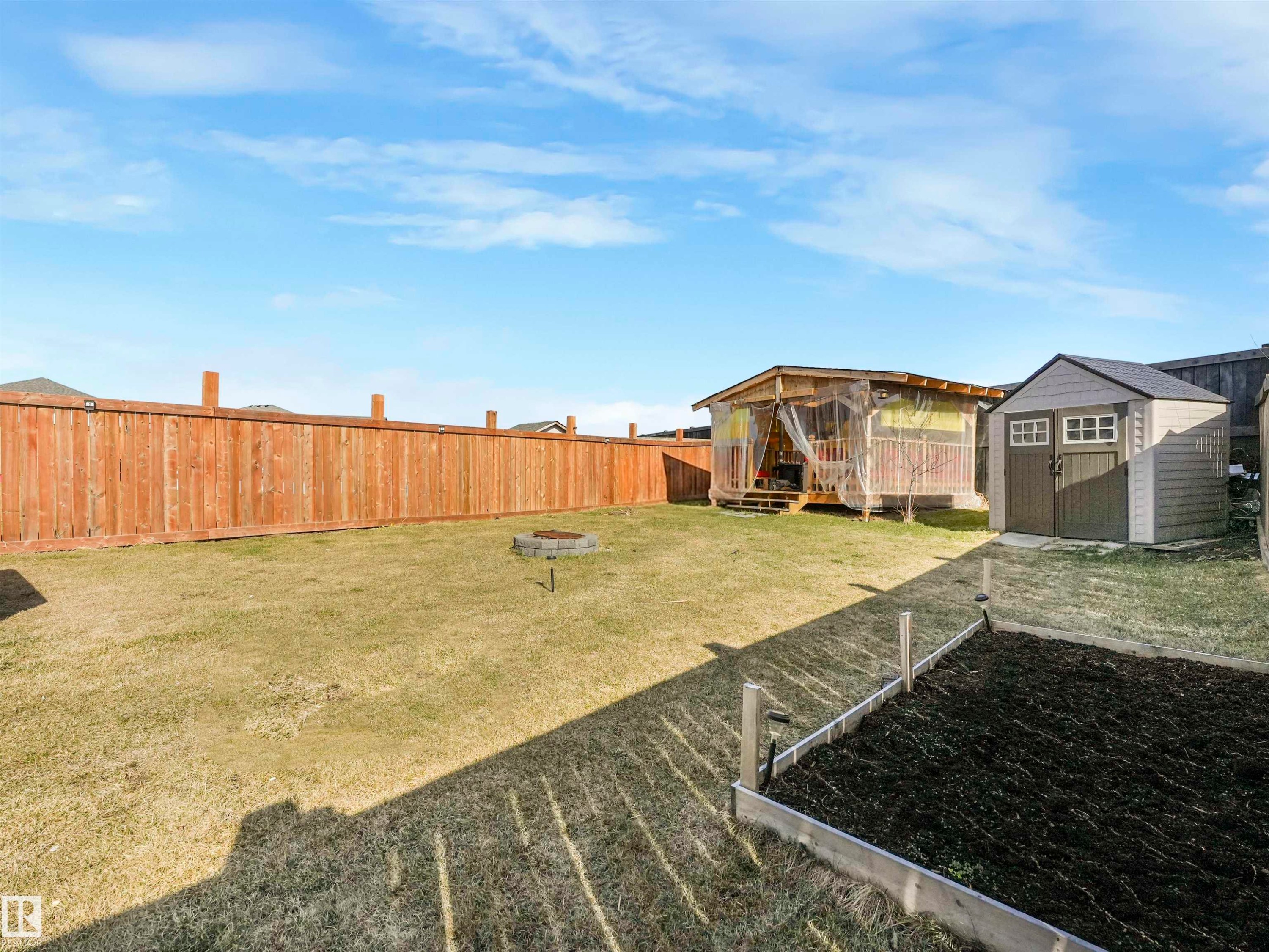 Expansive backyard featuring a privacy fence, a raised garden bed, a fire pit, a storage shed, and a covered deck structure - 17171 38 Street, Edmonton, AB
