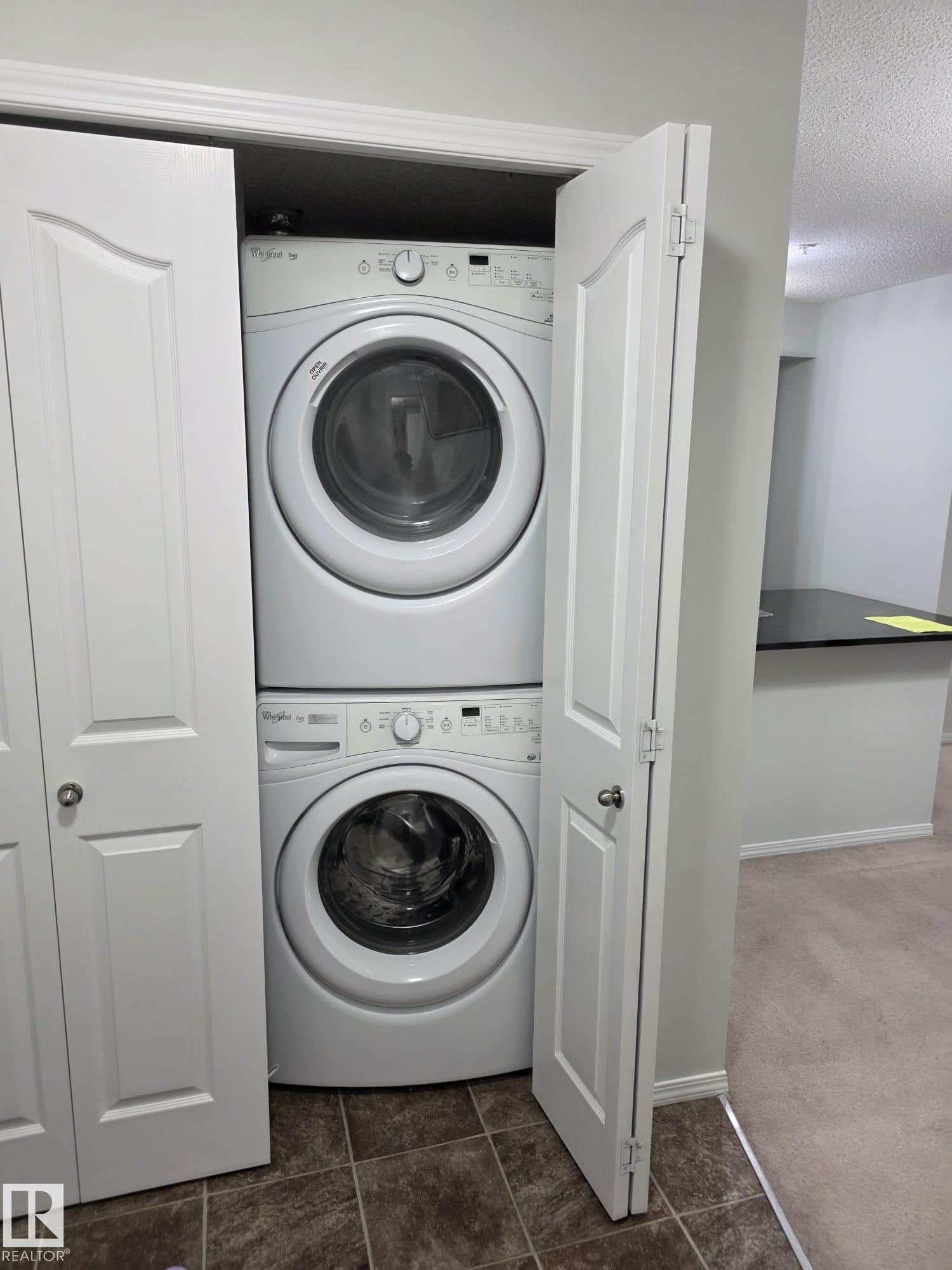 Dedicated laundry closet featuring a stacked washer and dryer, bifold doors, and tile flooring - 206 12045 22 Avenue, Edmonton, AB