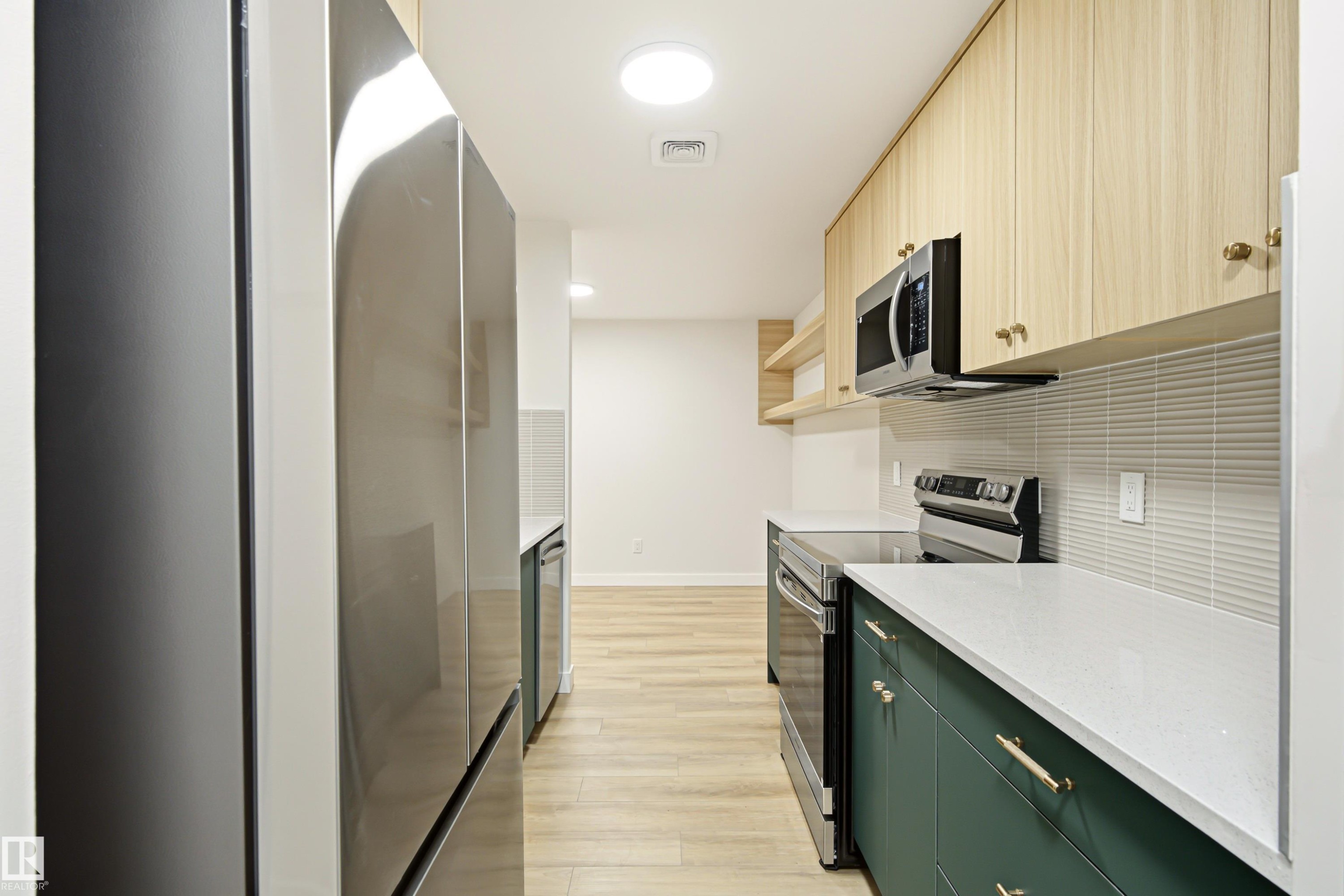 Modern galley kitchen featuring stainless steel appliances, light wood-finish flooring, white countertops, and a textured subway tile backsplash - 18217 84 Avenue Nw, Edmonton, AB
