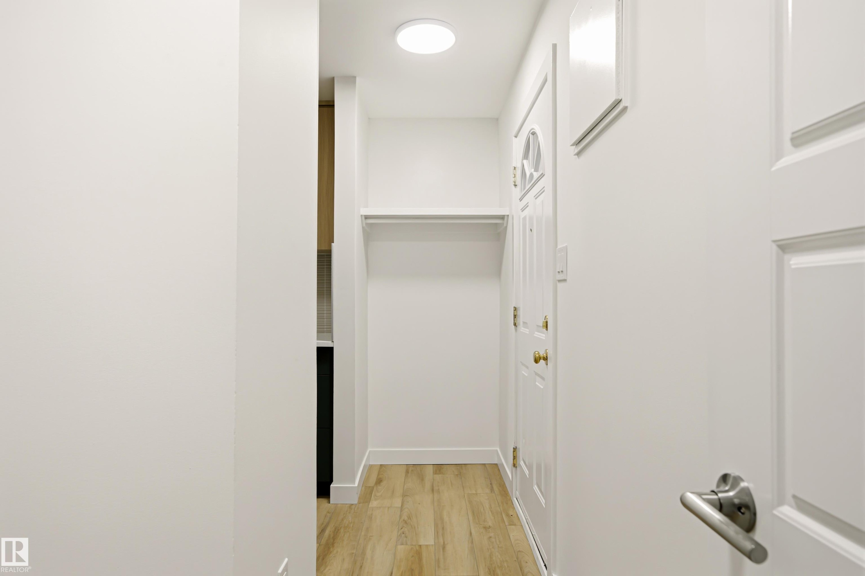 Foyer featuring light wood-finish flooring, a built-in coat rack with shelving, a white paneled front door with decorative glass, and a flush-mount ceiling light - 18217 84 Avenue Nw, Edmonton, AB