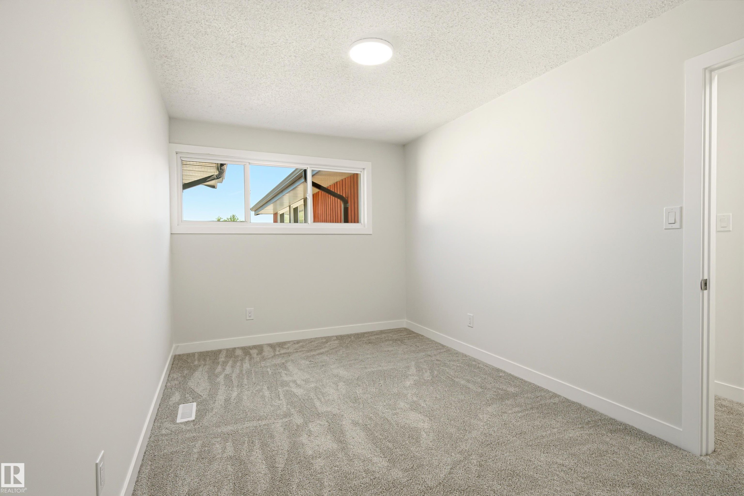Neutral-toned room featuring a single window, light gray carpeting, crisp white baseboards, and an overhead flush-mount light fixture - 18217 84 Avenue Nw, Edmonton, AB