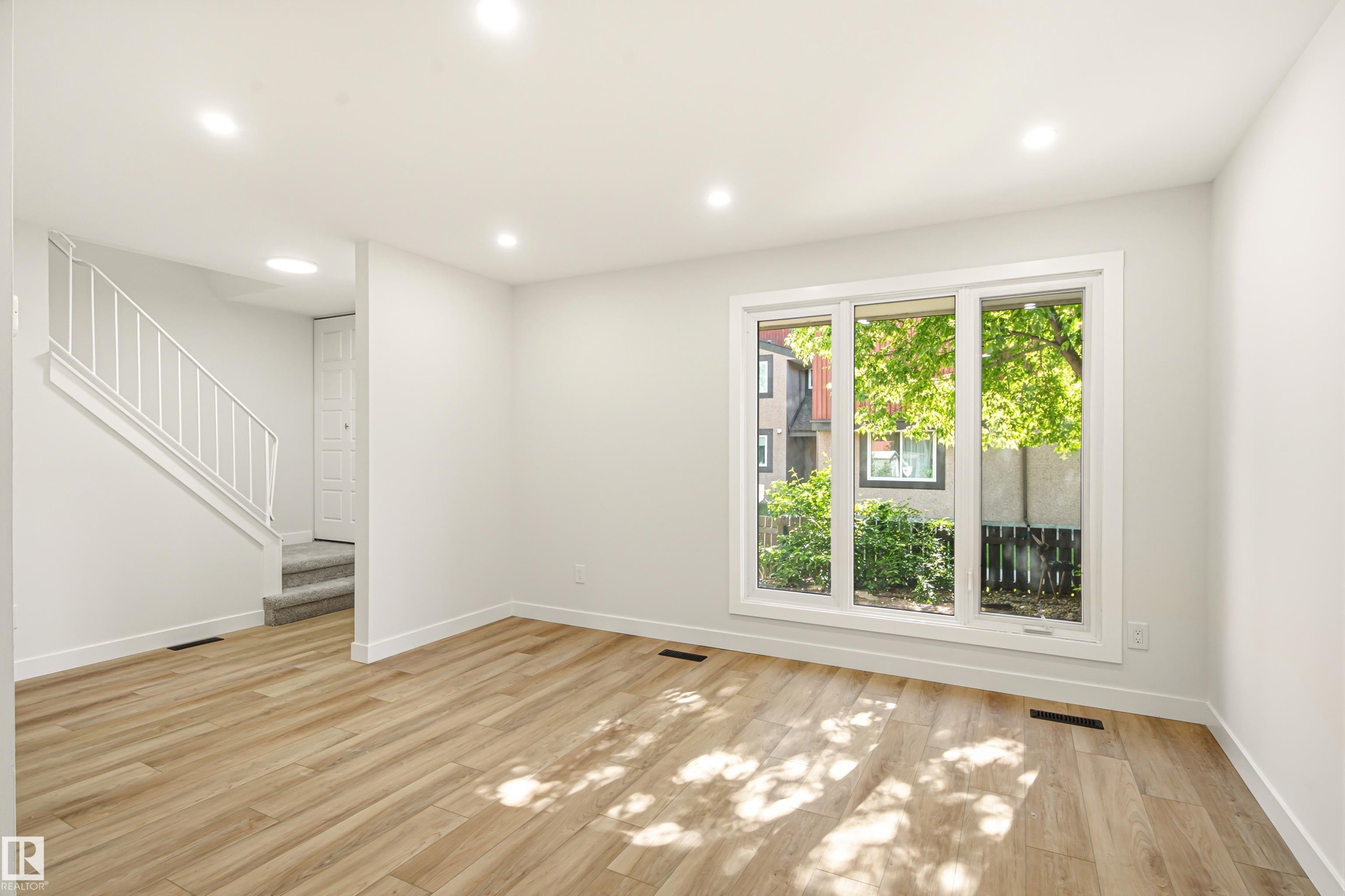 Bright living space featuring wood-finish flooring, recessed lighting, and a large multi-pane window - 18217 84 Avenue Nw, Edmonton, AB