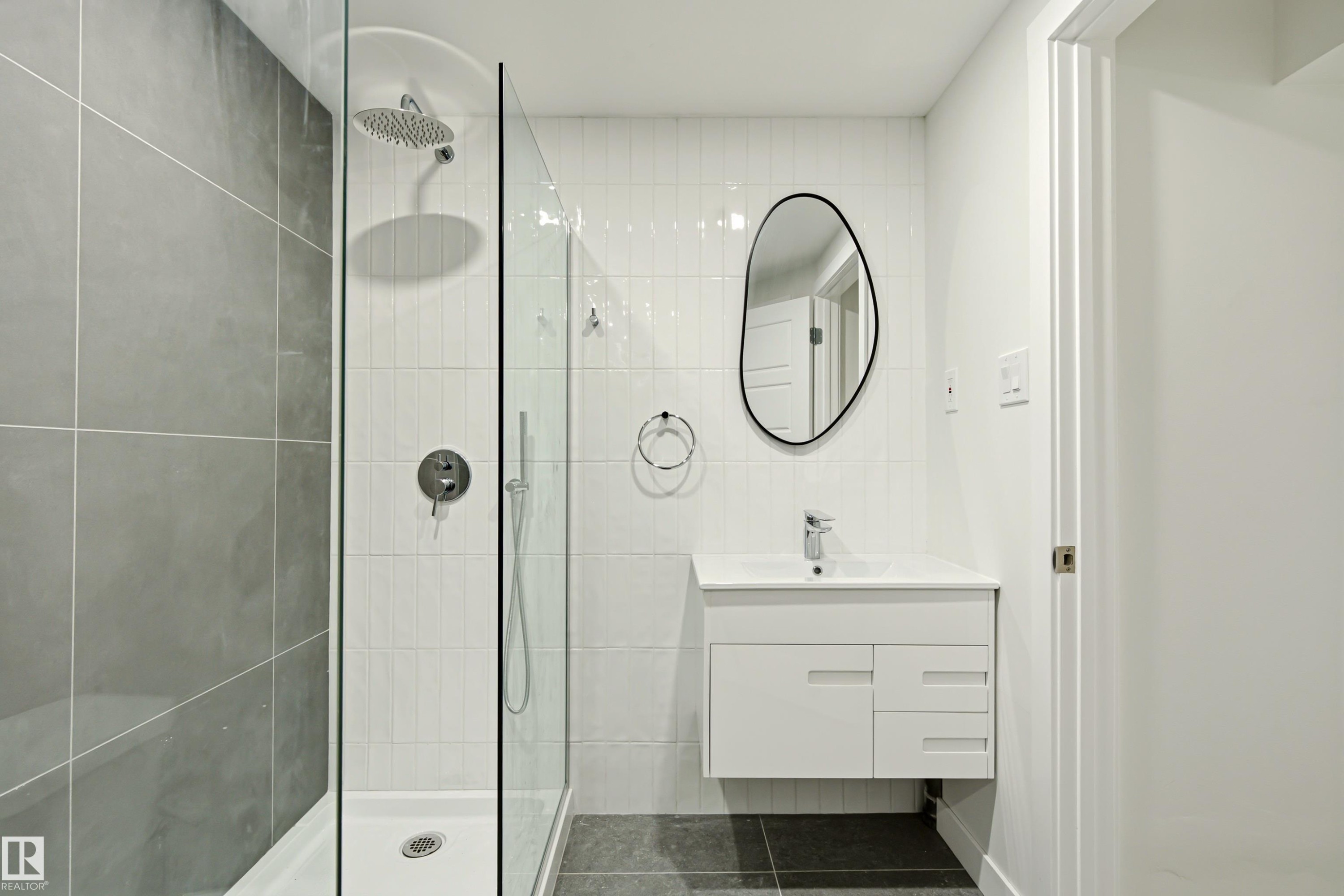 Contemporary bathroom featuring a frameless glass shower enclosure, a rainfall showerhead, and a wall-mounted vanity with integrated sink - 18217 84 Avenue Nw, Edmonton, AB