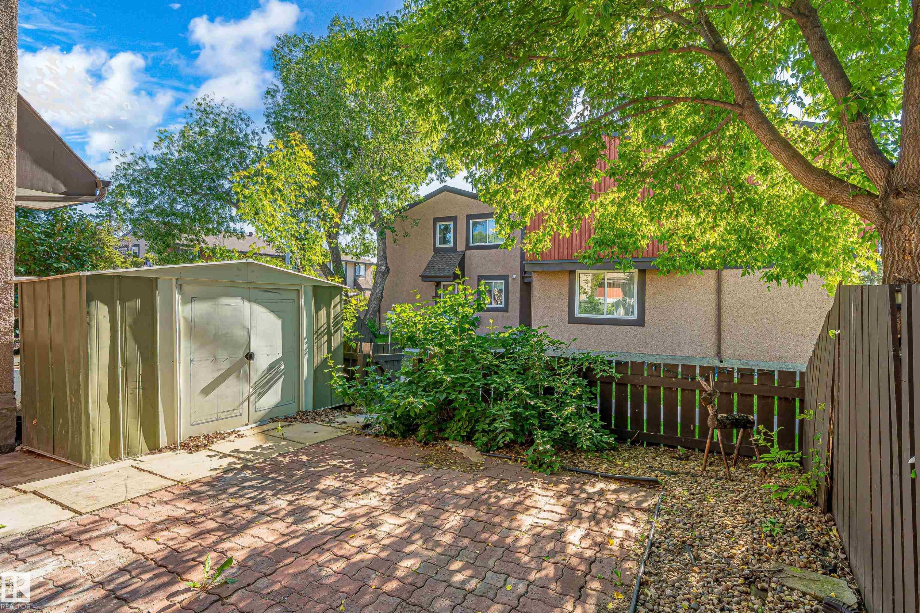 Brick paver patio area featuring a metal storage shed, mature trees, and privacy fencing - 18217 84 Avenue Nw, Edmonton, AB