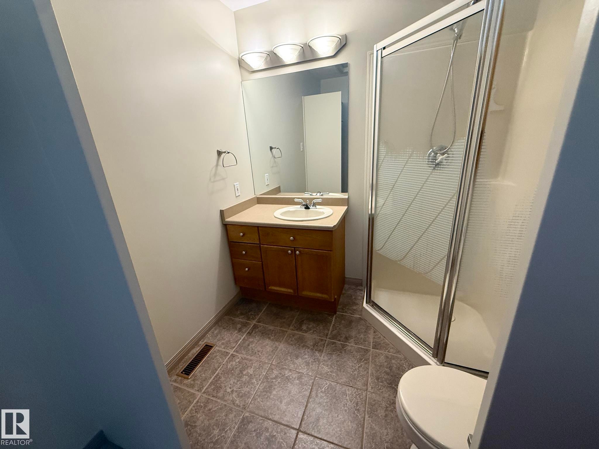 Bathroom featuring a vanity with an integrated sink, shower stall with clear glass enclosure, and tiled flooring - 1978 Tomlinson Green Green, Edmonton, AB