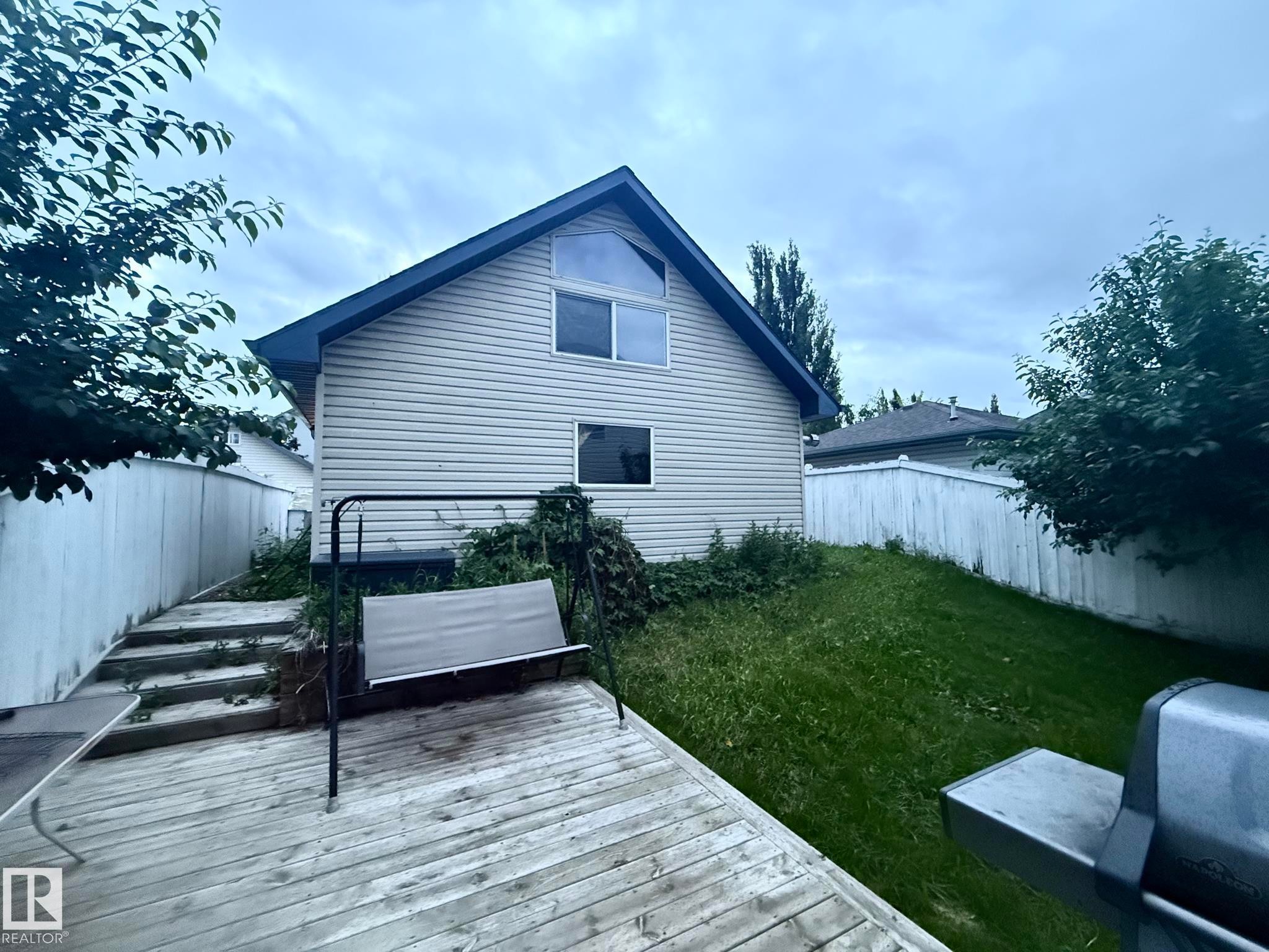 Rear exterior featuring a wood deck, sloped lawn, and perimeter fencing - 1978 Tomlinson Green Green, Edmonton, AB