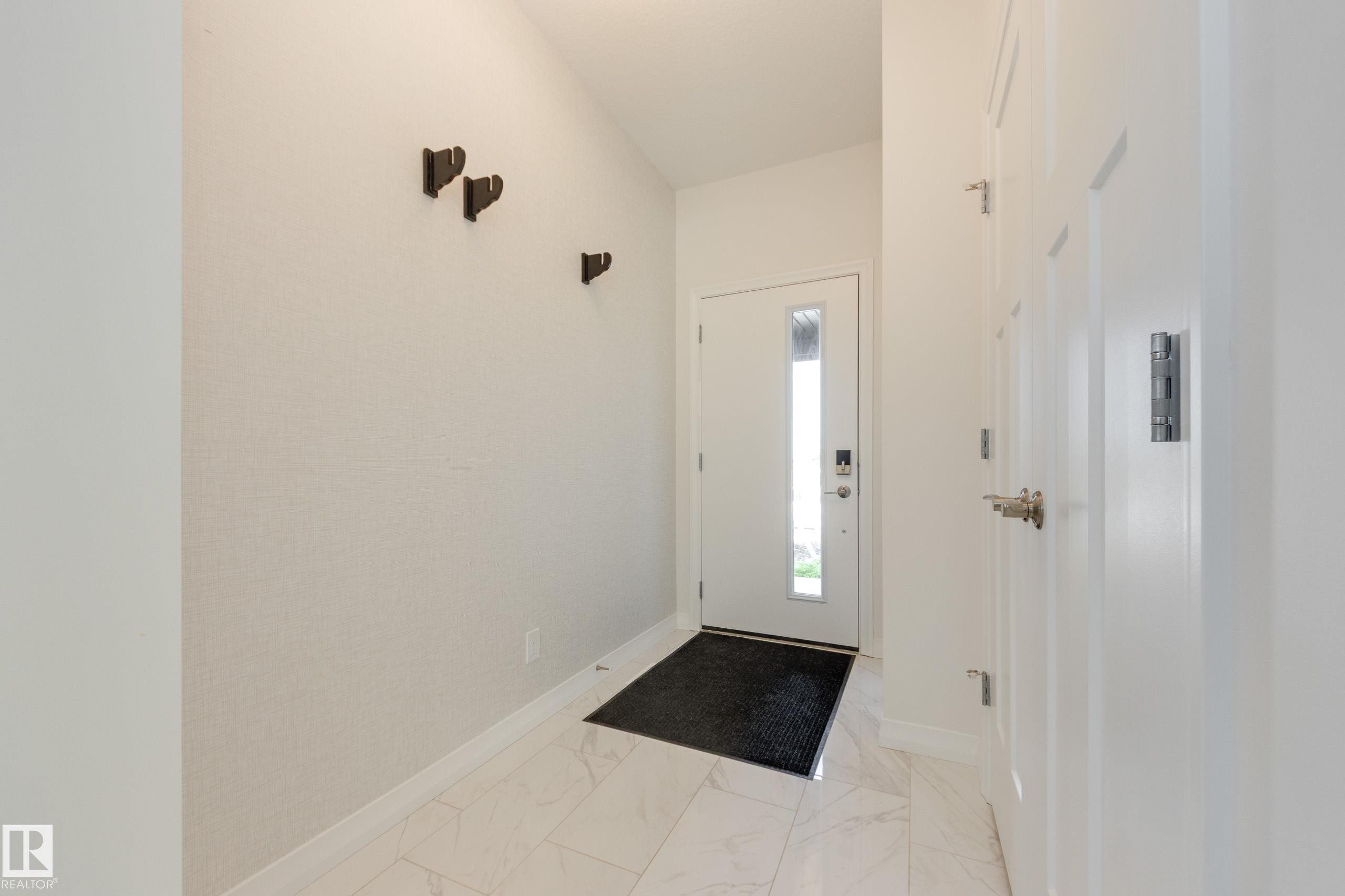 Entryway featuring white panel doors, modern door hardware, wall-mounted coat hooks, and white tile flooring - 3249 Dixon Way Sw, Edmonton, AB