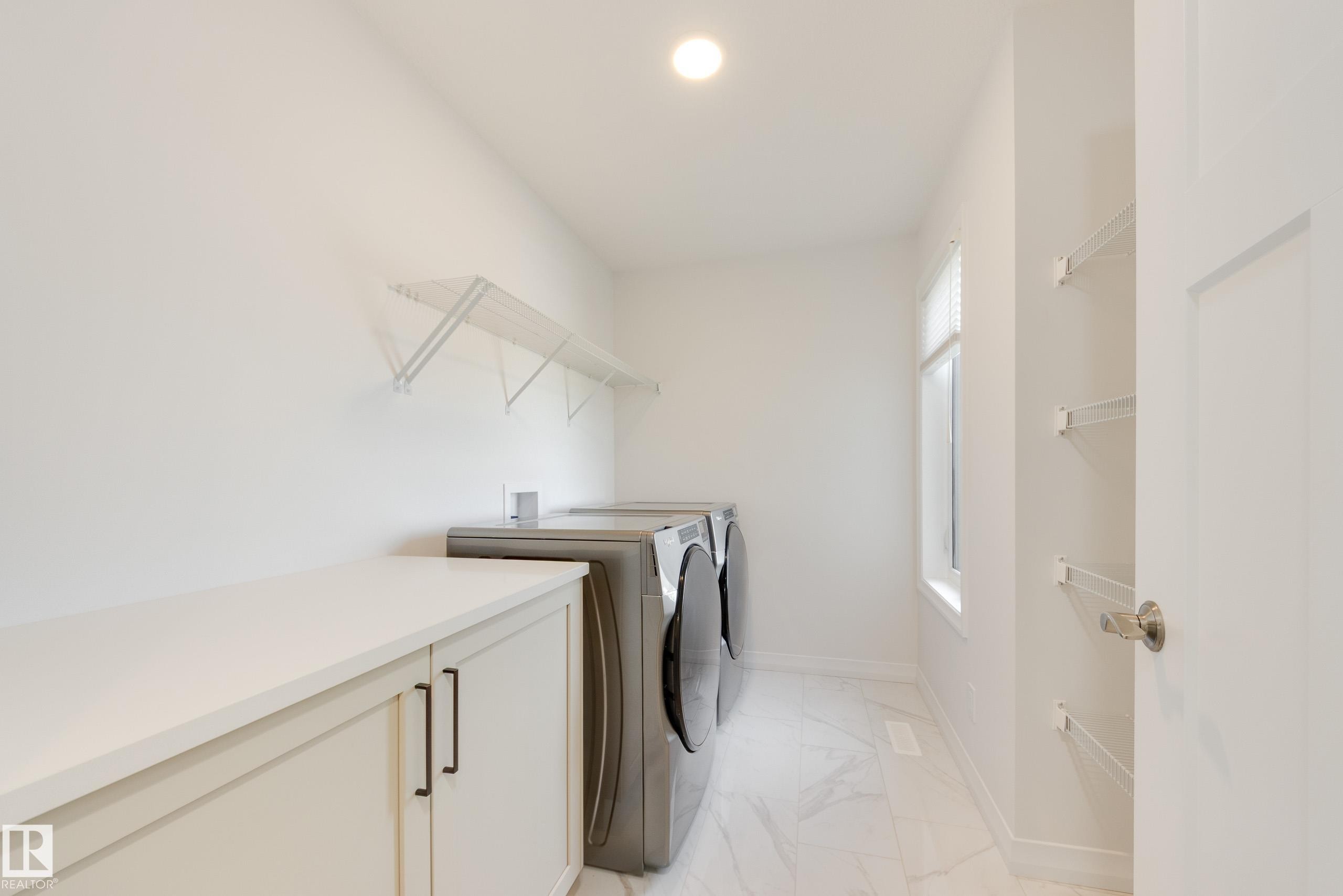 Dedicated laundry area featuring a built-in countertop, light-toned cabinetry with dark hardware, a window for natural light, and tile flooring - 3249 Dixon Way Sw, Edmonton, AB