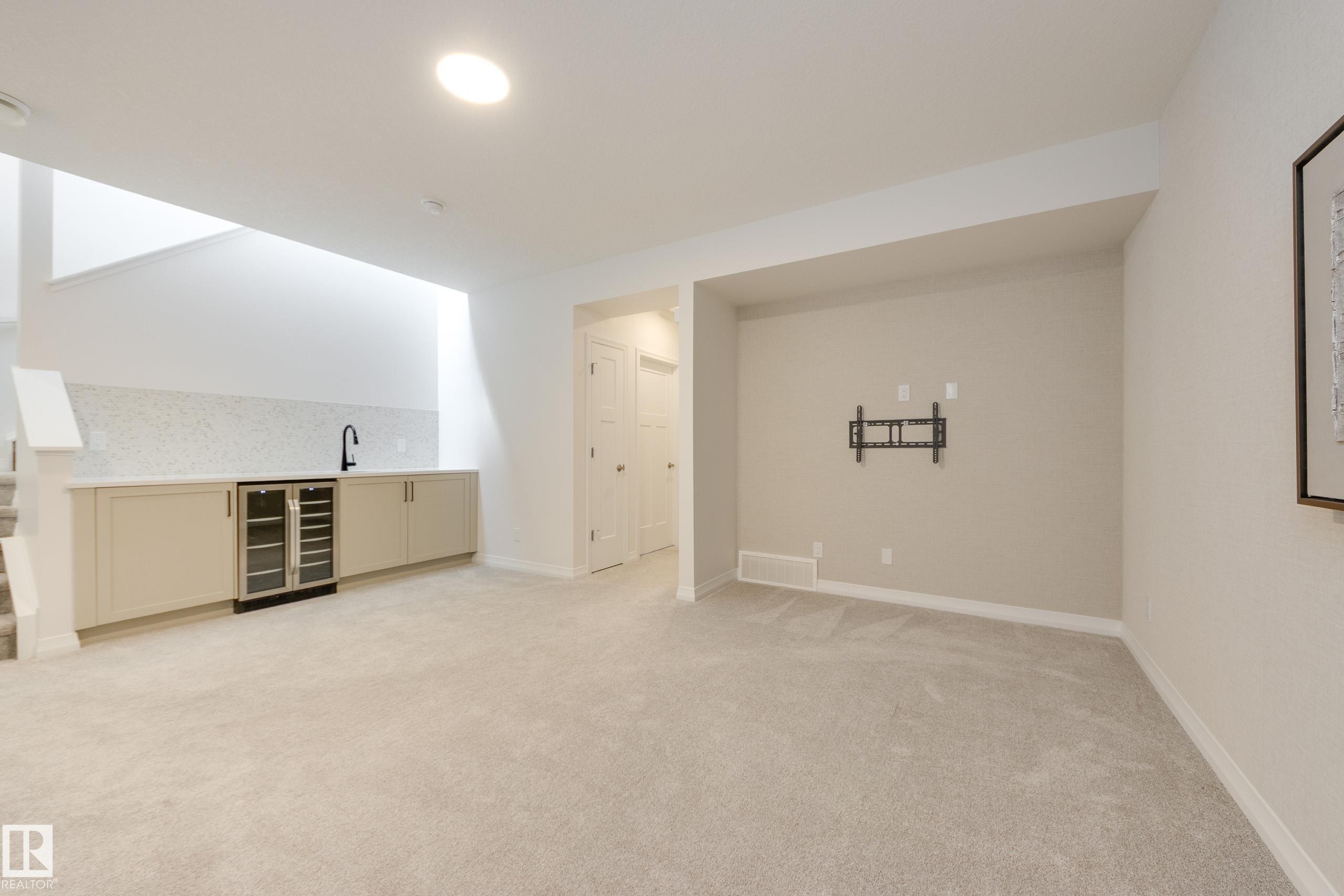 Finished lower-level space featuring light-colored carpeting and a built-in wet bar with a beverage cooler - 3249 Dixon Way Sw, Edmonton, AB