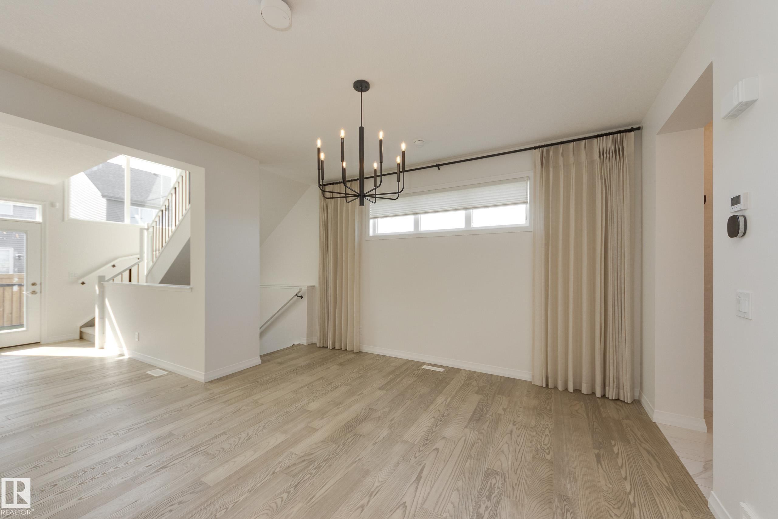 Spacious interior featuring wood-finish flooring, a modern black chandelier, and white window blinds - 3249 Dixon Way Sw, Edmonton, AB