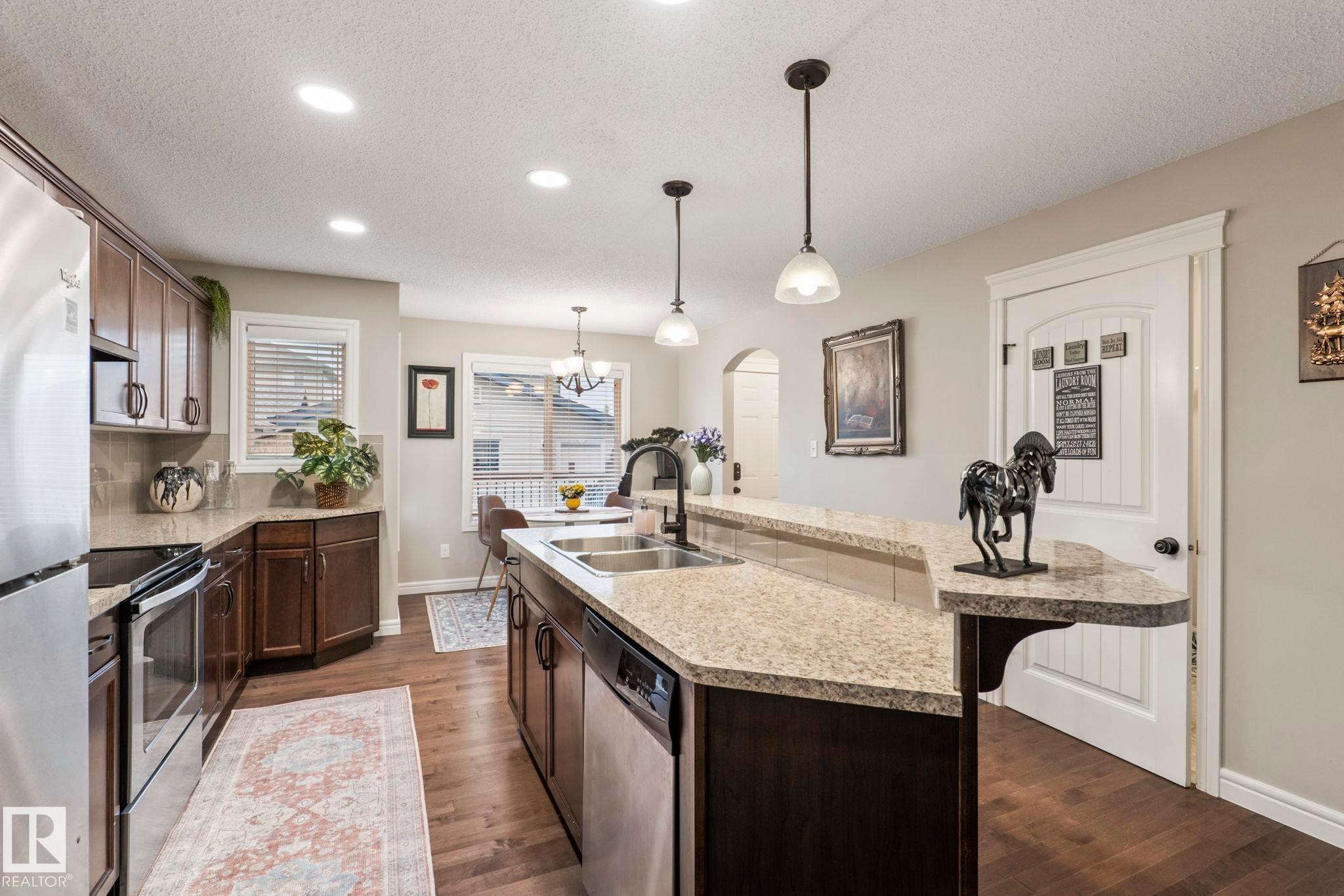 Kitchen with wood-finish flooring, recessed lighting, and a peninsula featuring a double basin sink with a high-arch faucet - 1542 33A St Nw, Edmonton, AB