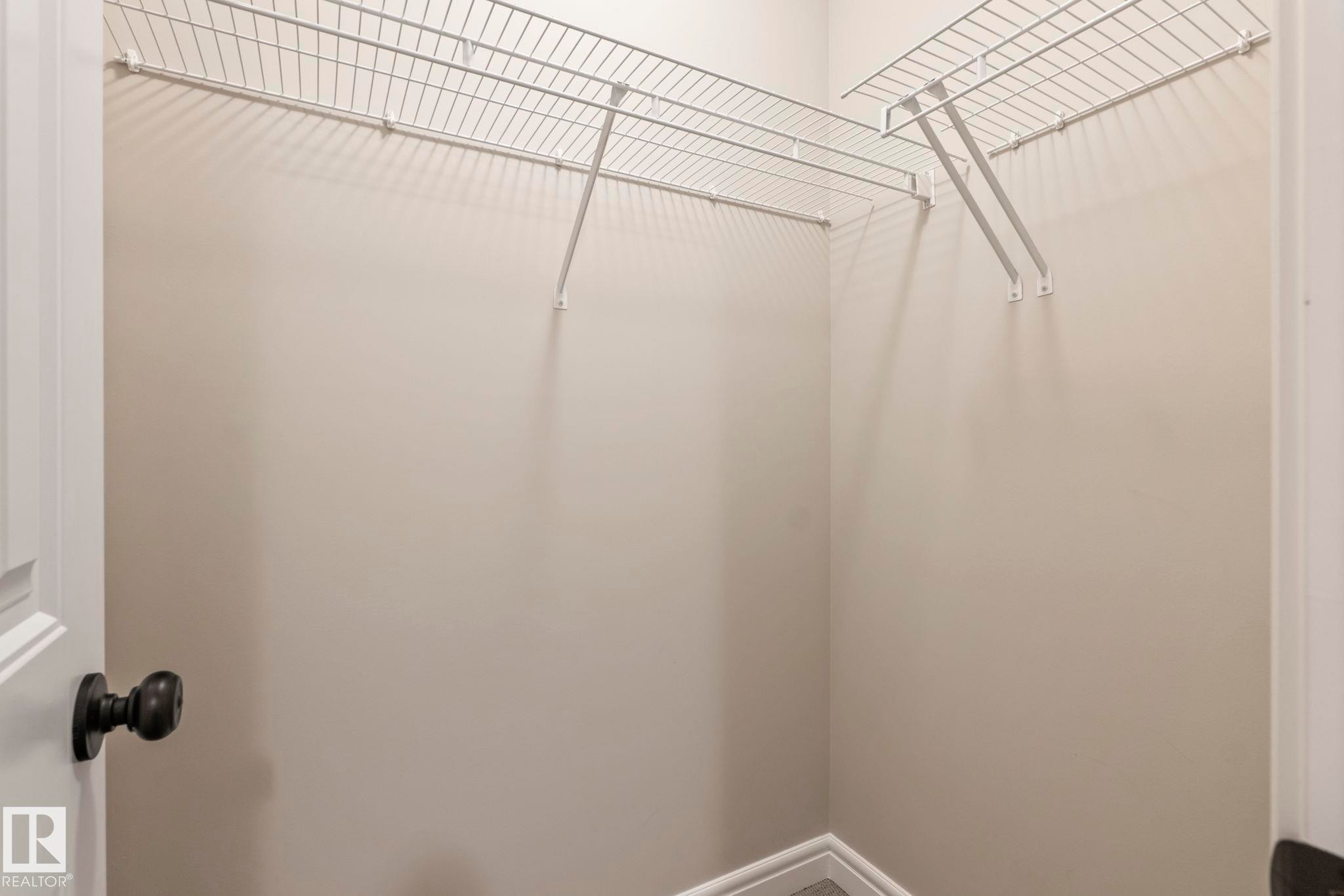Walk-in closet featuring wire shelving, neutral wall paint, white trim, and wood-finish flooring - 1542 33A St Nw, Edmonton, AB