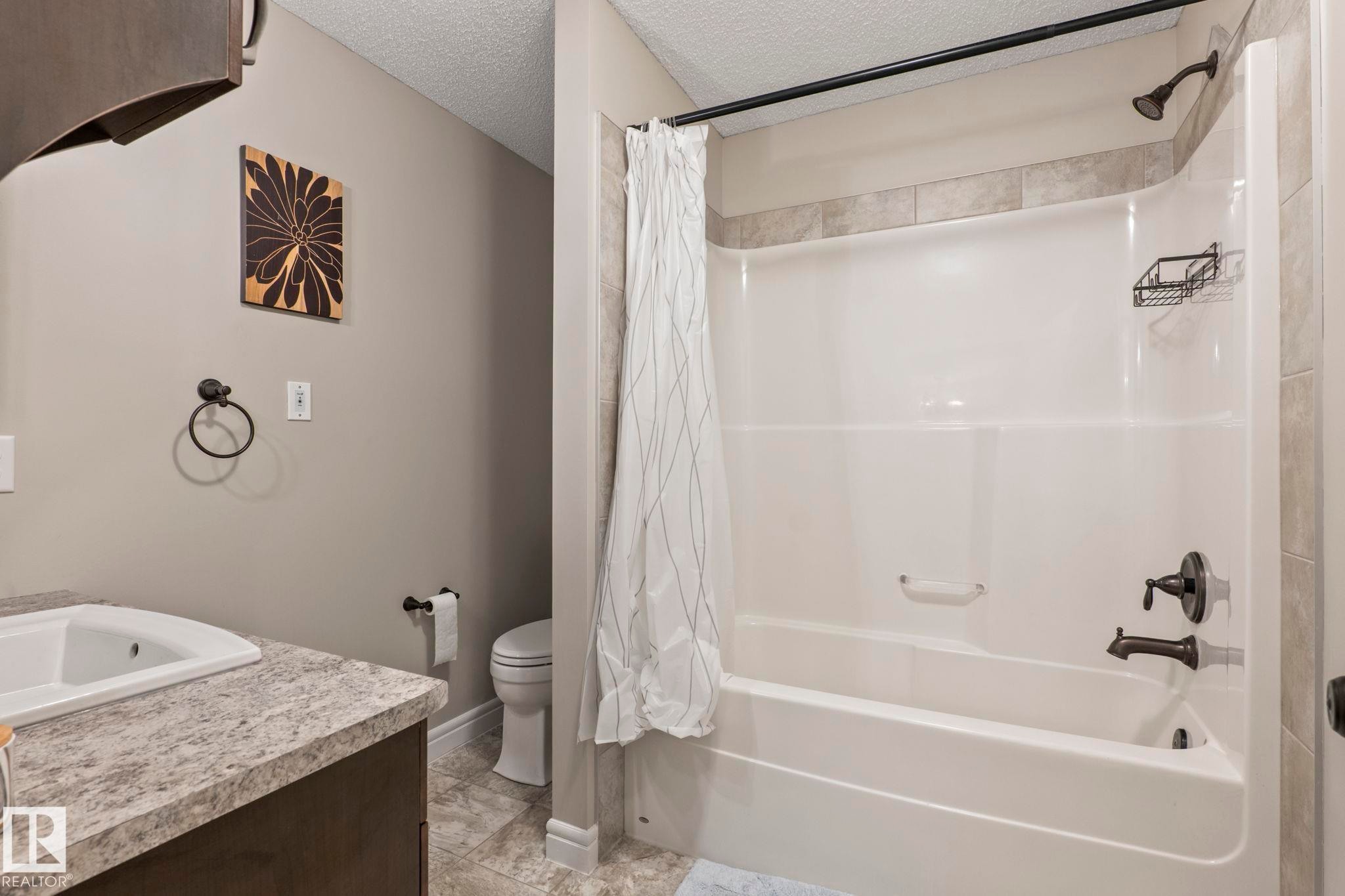 Bathroom featuring a white shower-tub combination with a dark-toned showerhead and faucet, set against tile surround - 1542 33A St Nw, Edmonton, AB