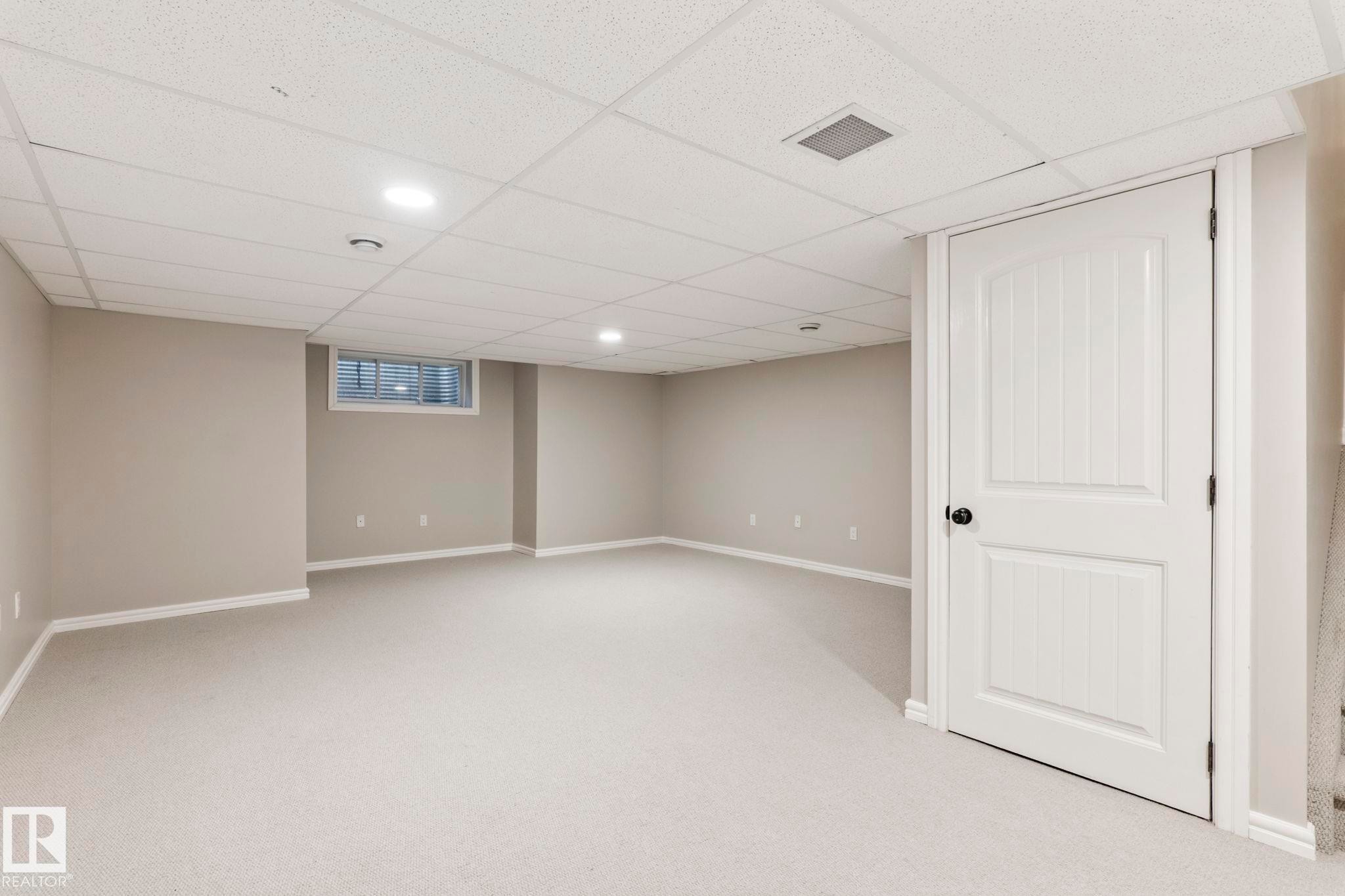 Spacious finished room featuring light gray carpeting, neutral wall paint, white trim, recessed lighting, and a drop ceiling - 1542 33A St Nw, Edmonton, AB