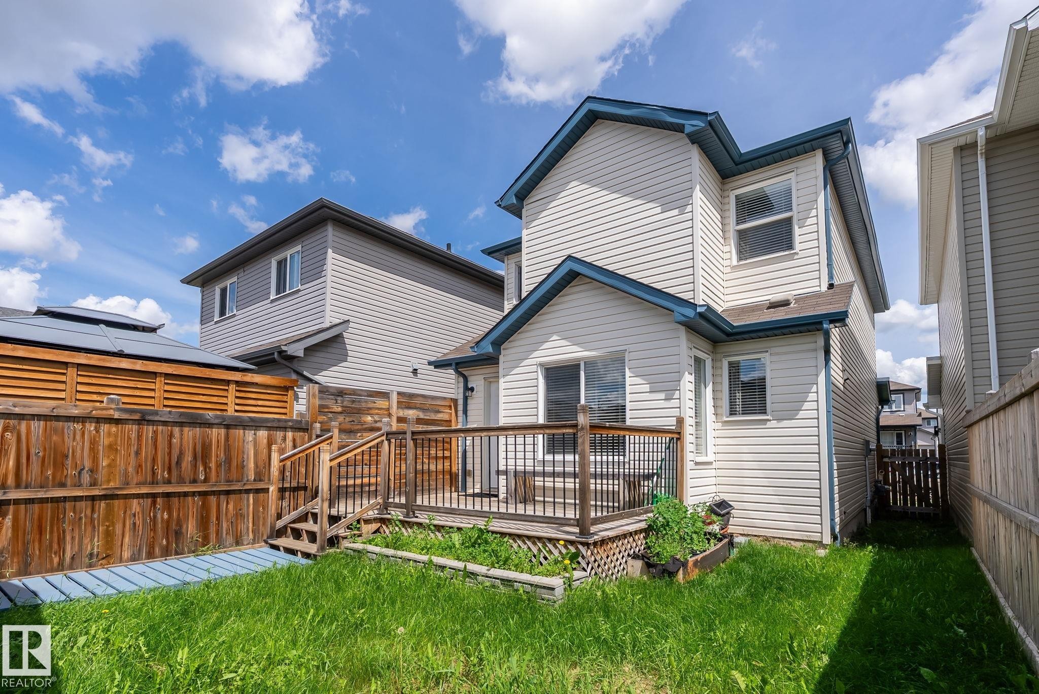 Rear exterior featuring a ground-level deck, wood fencing, and a grassy yard space - 1542 33A St Nw, Edmonton, AB