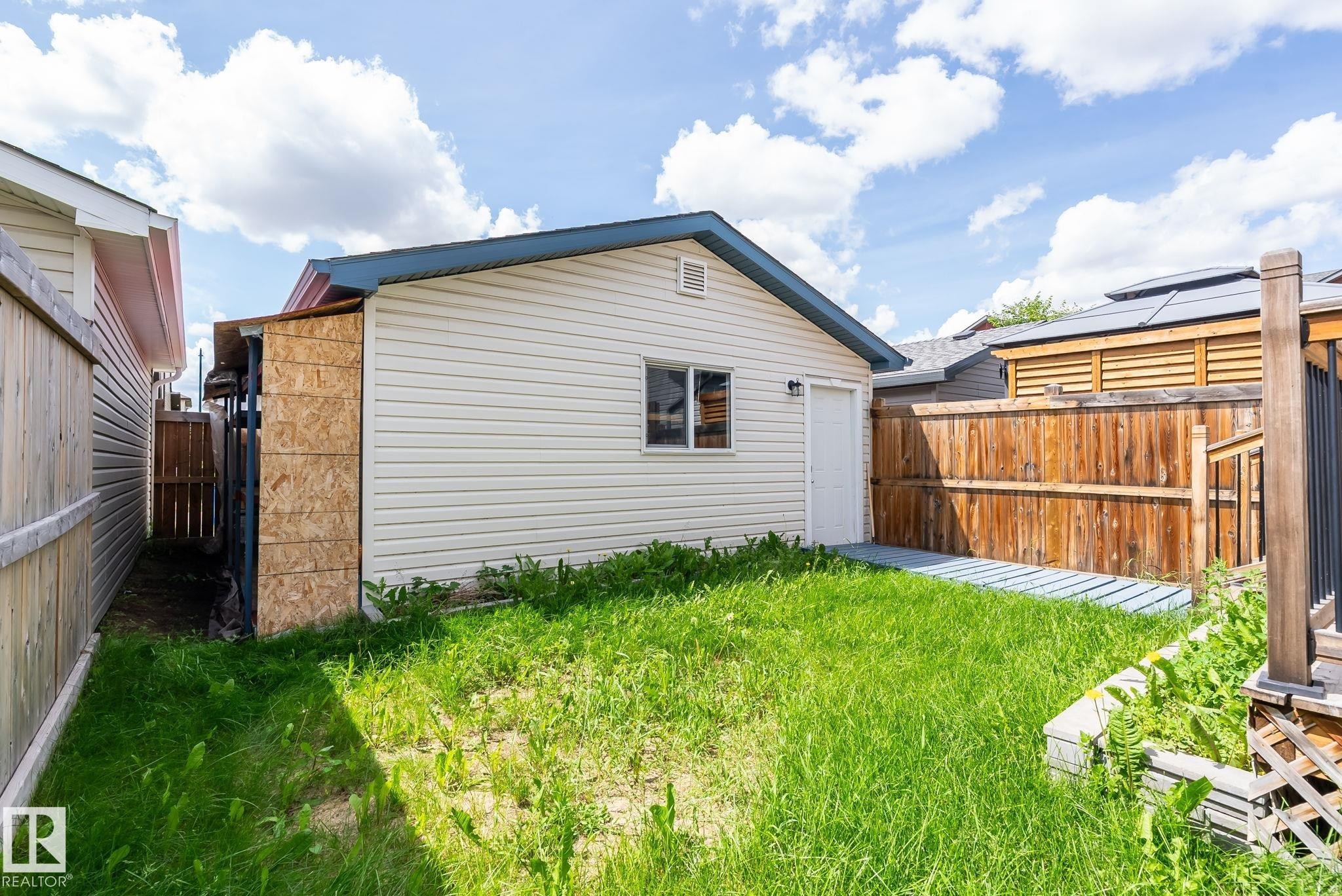 Freestanding outbuilding with horizontal siding and a single window, featuring a metal roof and an attached lean-to structure - 1542 33A St Nw, Edmonton, AB