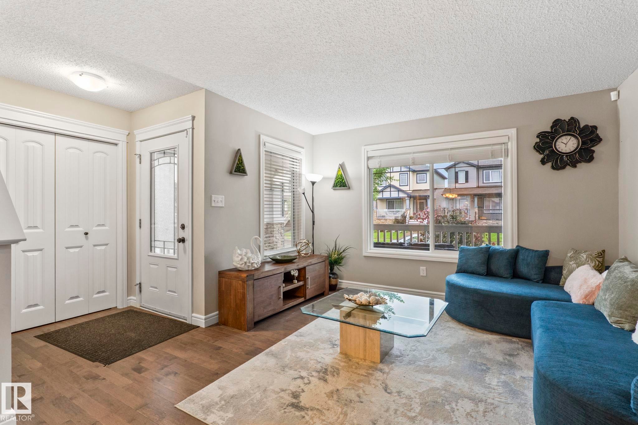 Entryway and living area featuring wood-finish flooring, a white paneled front door with decorative glass inserts, and a closet with bifold doors - 1542 33A St Nw, Edmonton, AB