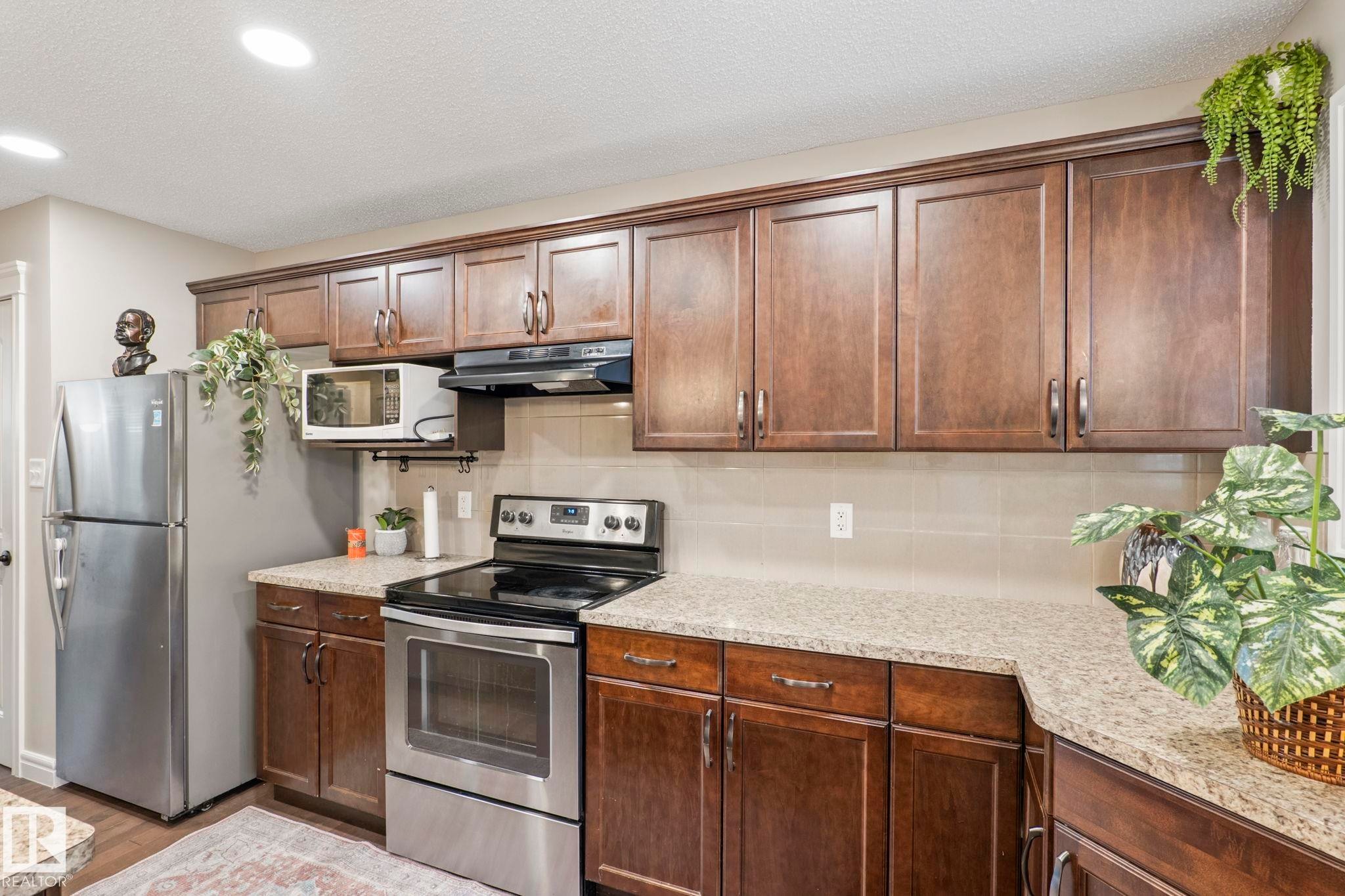 Kitchen featuring extensive wood cabinetry with modern hardware, speckled countertops, and stainless steel appliances - 1542 33A St Nw, Edmonton, AB