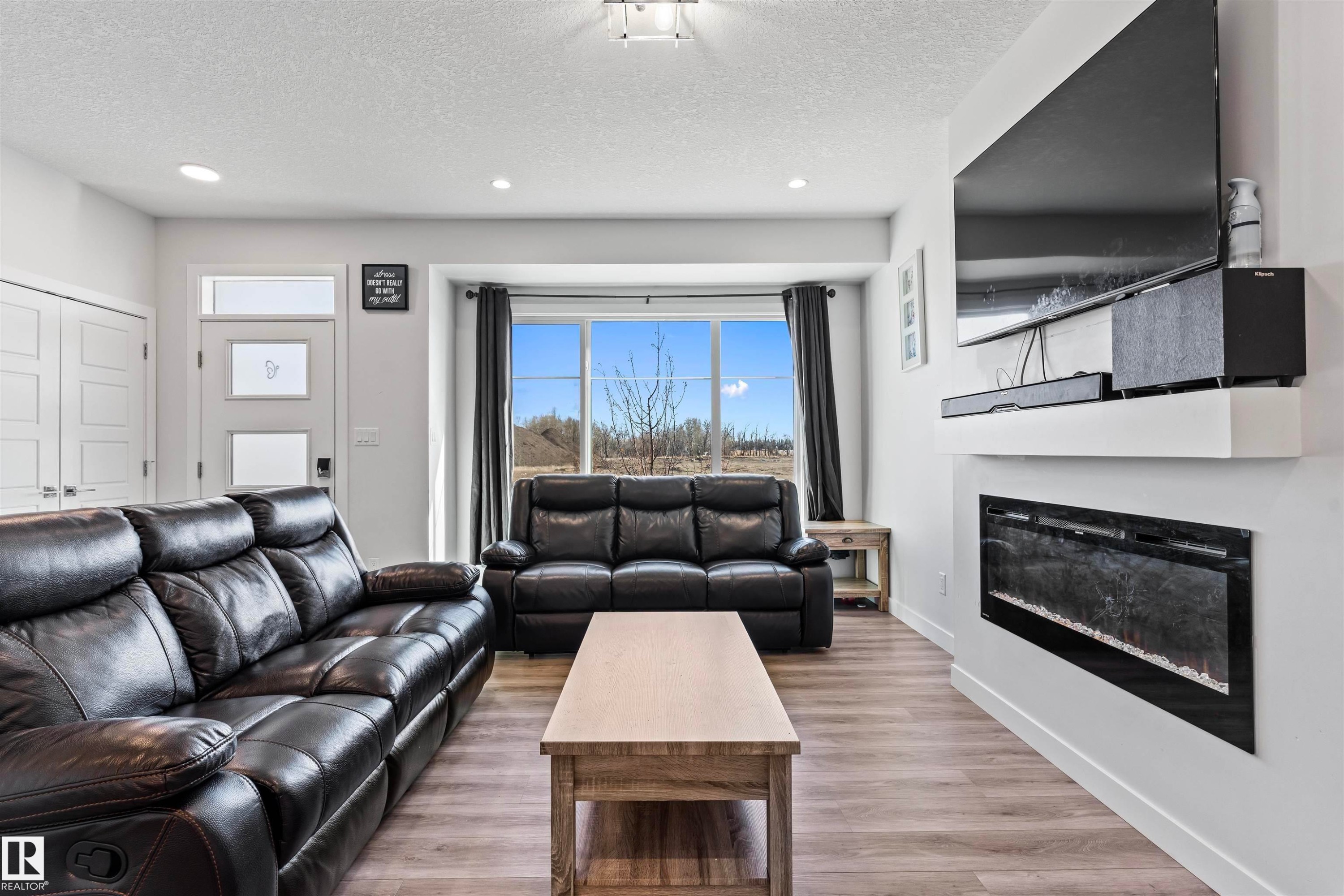 Living area featuring light wood-finish flooring, recessed lighting, and a wide window with dark drapery - 8046 Kiriak Link, Edmonton, AB - Indoor Photo Showing Living Room With Fireplace