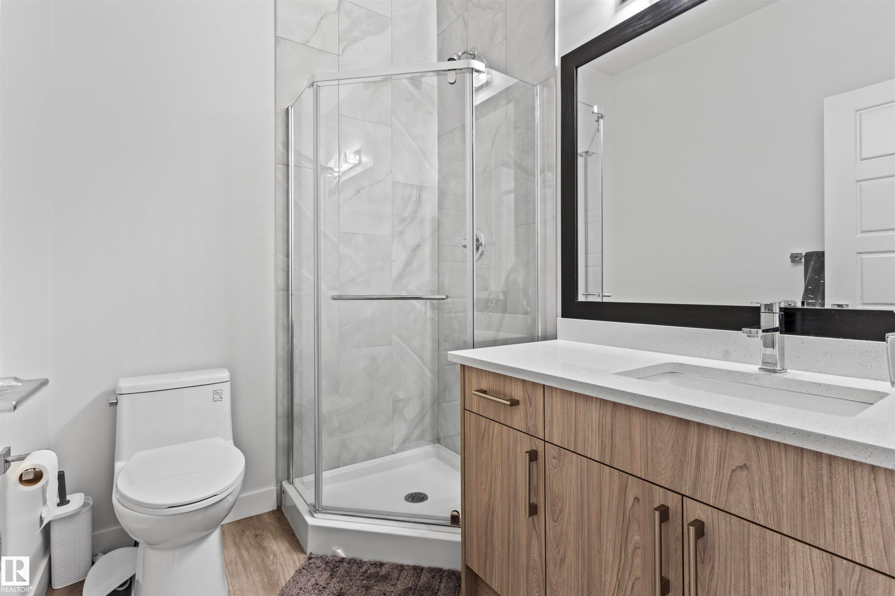 Bathroom featuring a glass-enclosed corner shower with marble-look tile surround, a single vanity with wood-finish cabinetry, a white countertop, and an integrated rectangular sink - 8046 Kiriak Link, Edmonton, AB - Indoor Photo Showing Bathroom