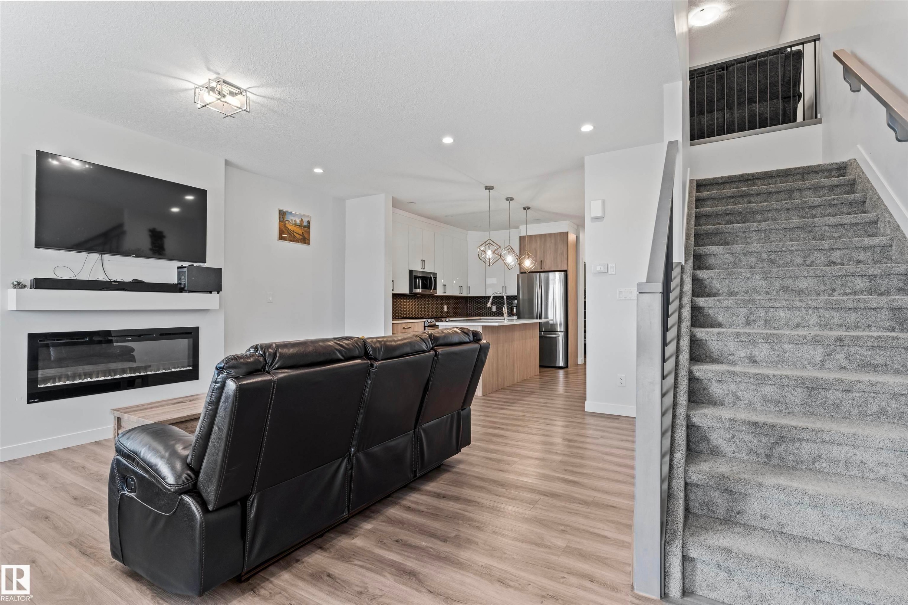 Open-concept living area featuring wood-finish flooring, an electric fireplace with a white mantel, and recessed lighting - 8046 Kiriak Link, Edmonton, AB - Indoor With Fireplace