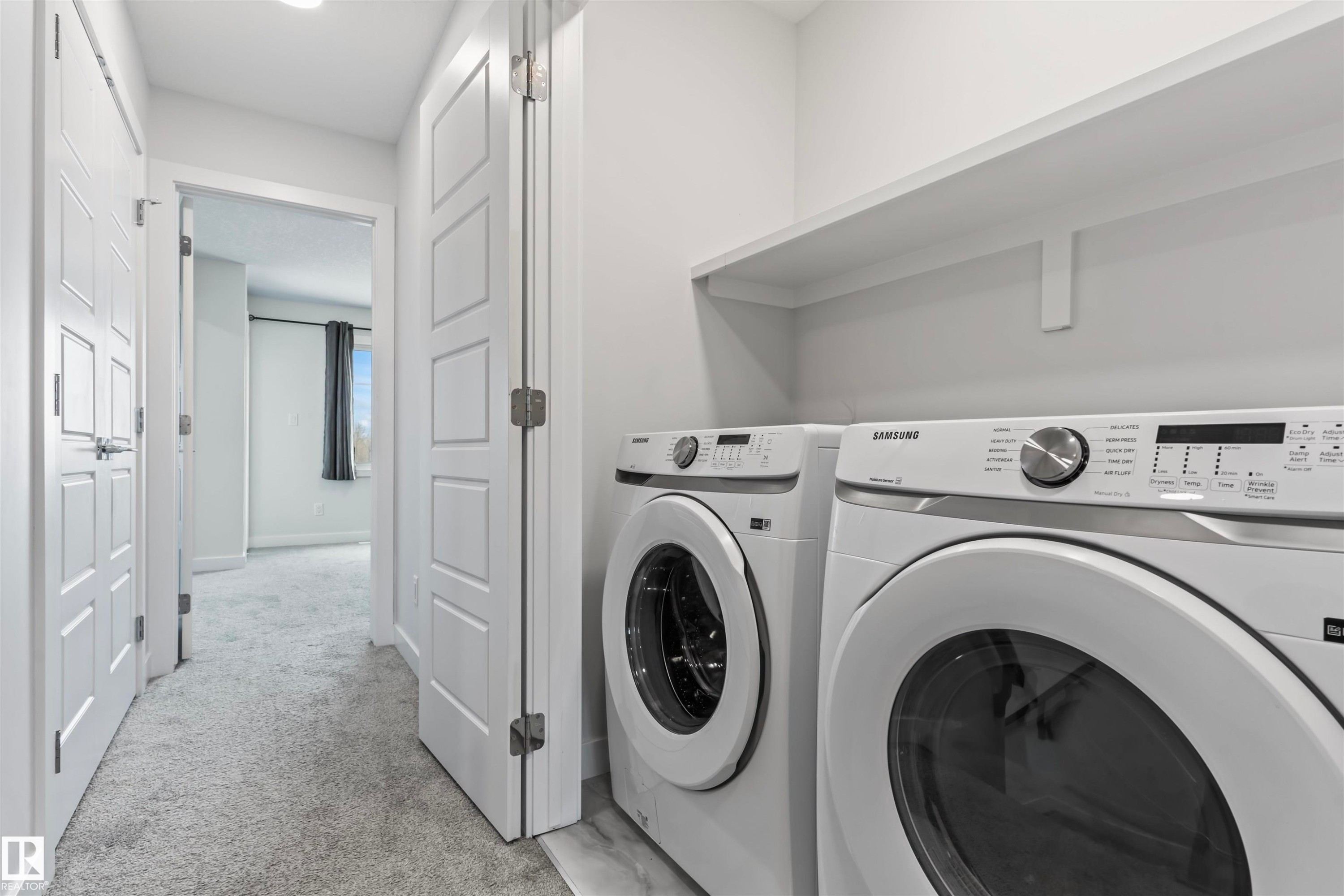 Dedicated laundry area featuring front-loading washer and dryer units, a full-width upper shelf, and light wood-finish flooring - 8046 Kiriak Link, Edmonton, AB - Indoor Photo Showing Laundry Room