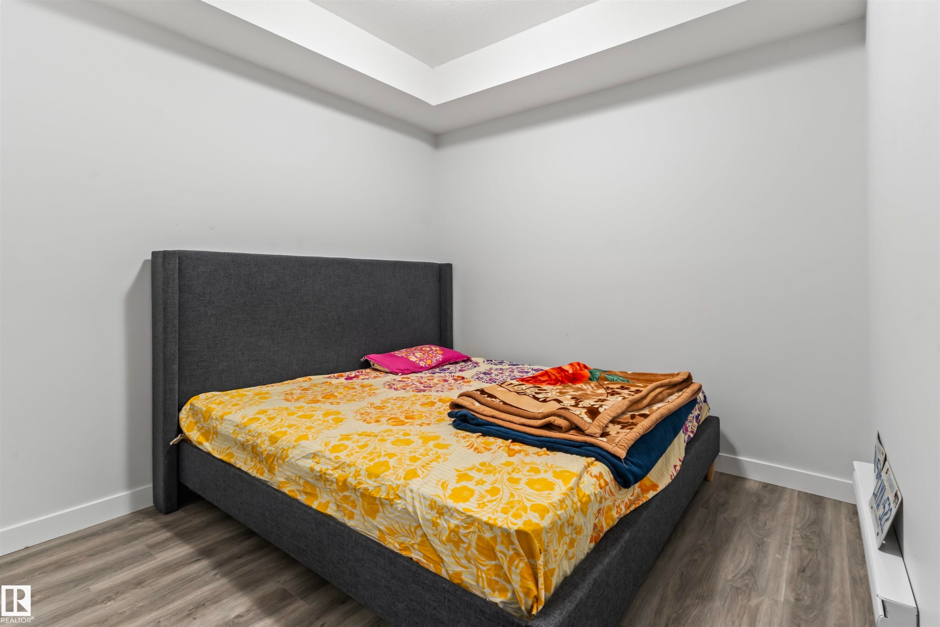 Room featuring contemporary light gray walls, wood-finish flooring, white baseboards, and a tray ceiling detail - 8046 Kiriak Link, Edmonton, AB - Indoor Photo Showing Bedroom