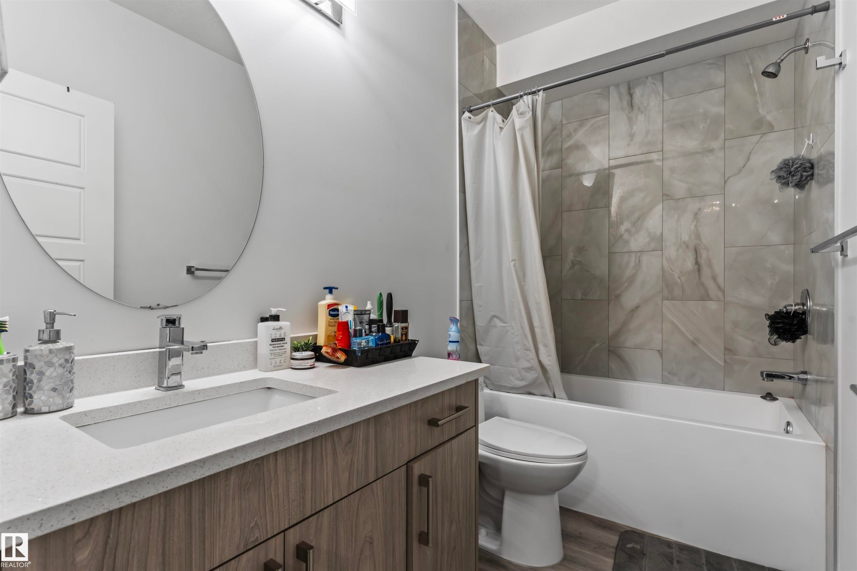 Full bathroom featuring a rectangular undermount sink, a chrome single-handle faucet, and a large round mirror - 8046 Kiriak Link, Edmonton, AB - Indoor Photo Showing Bathroom