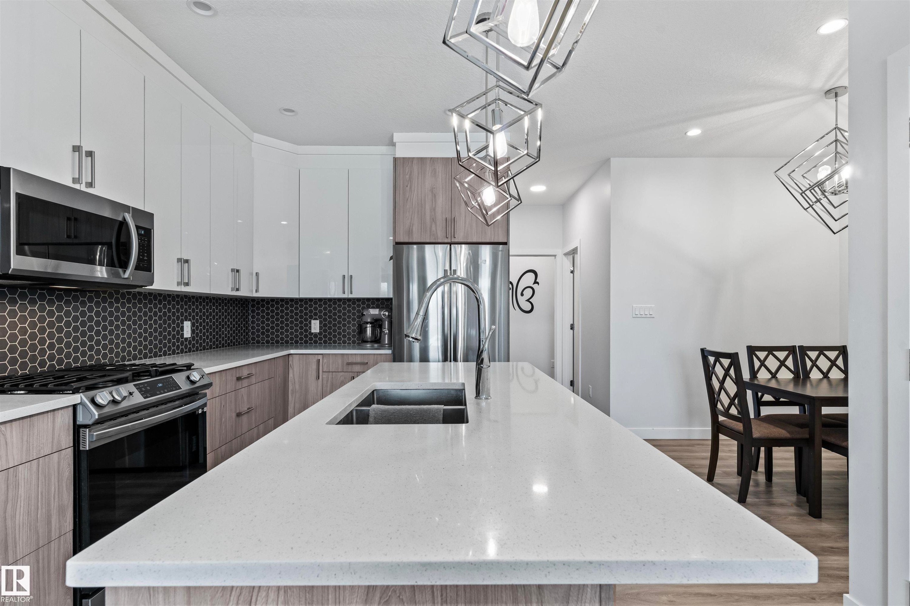 Contemporary kitchen featuring a large center island with an undermount sink, white countertops, and a dark hexagonal tile backsplash - 8046 Kiriak Link, Edmonton, AB - Indoor Photo Showing Kitchen With Double Sink With Upgraded Kitchen