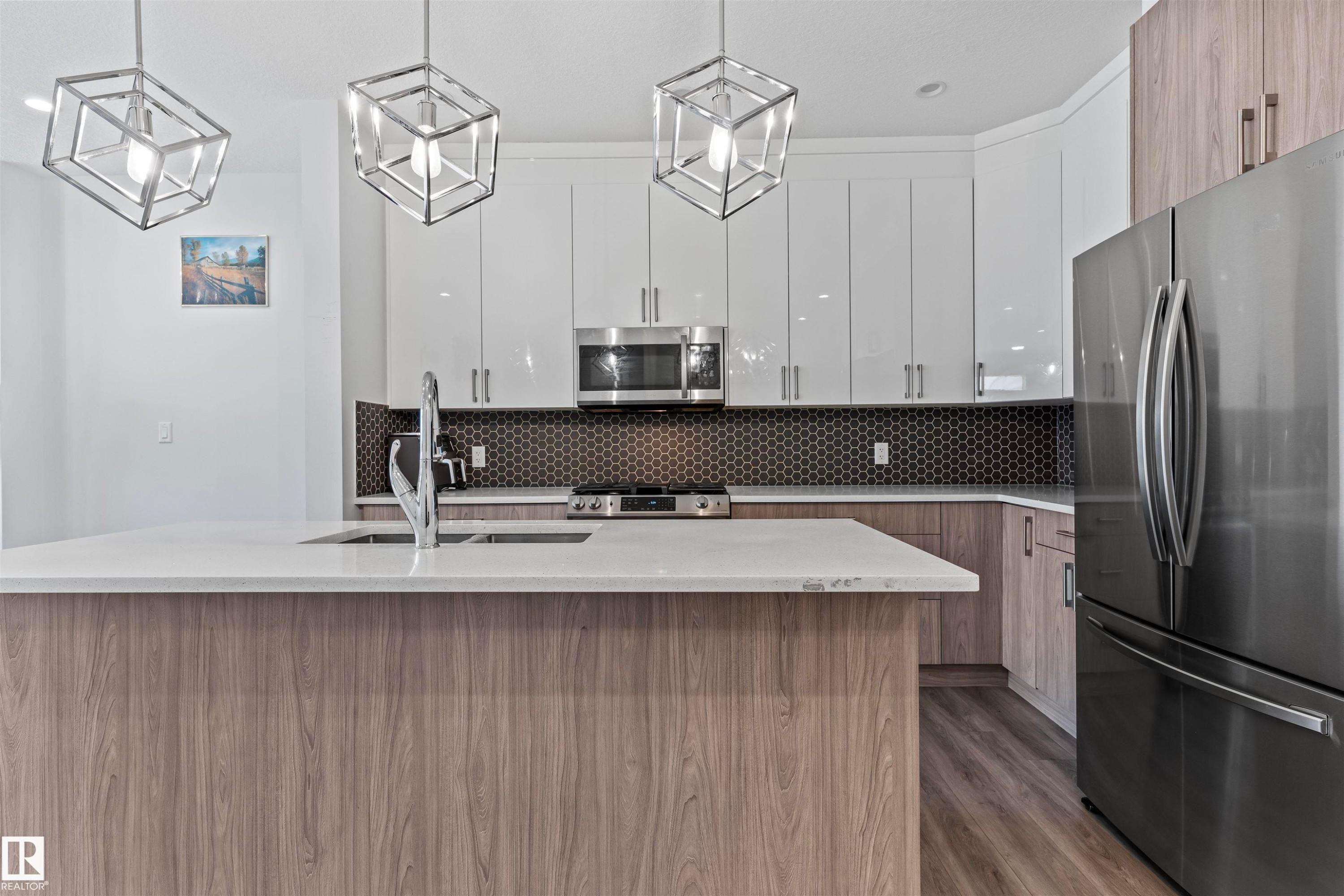 Gourmet kitchen featuring a wood-finish island with integrated sink, white countertops, stainless steel appliances, white upper cabinetry, and dark honeycomb tile backsplash - 8046 Kiriak Link, Edmonton, AB - Indoor Photo Showing Kitchen With Upgraded Kitchen