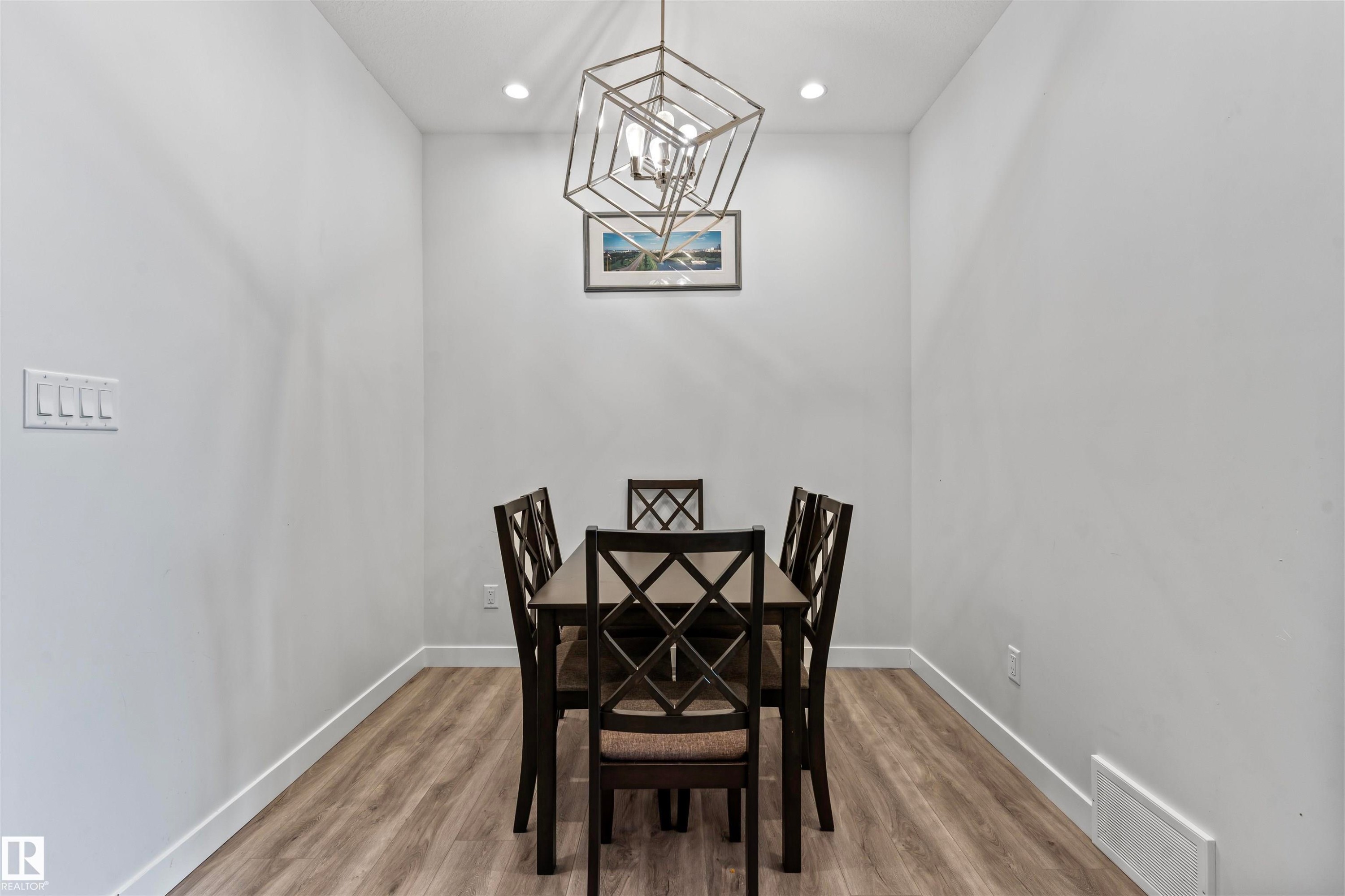 Recessed dining area featuring light wood-finish flooring, white baseboards, and a contemporary geometric chandelier - 8046 Kiriak Link, Edmonton, AB - Indoor Photo Showing Dining Room