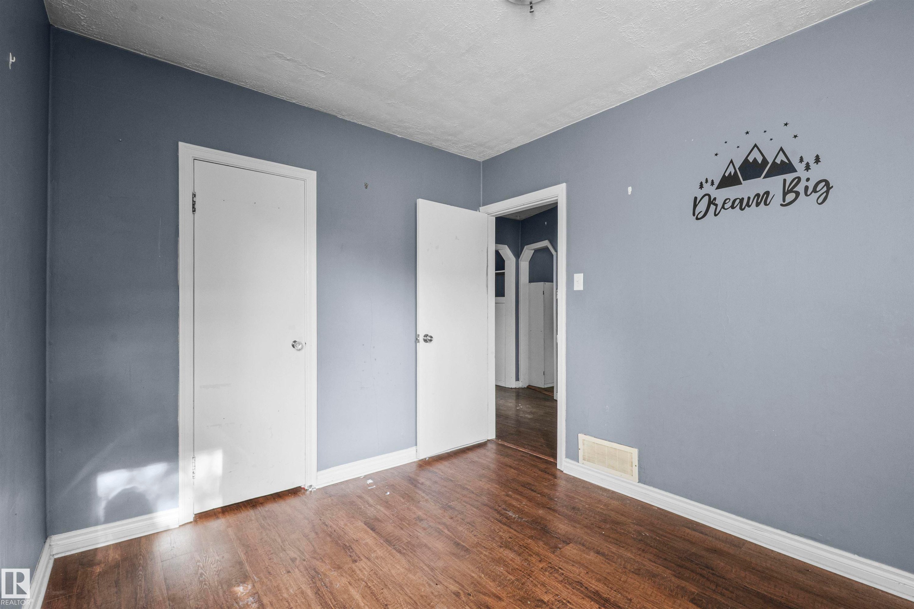 Interior room featuring wood-finish flooring, light blue-gray walls, white trim, and two white doors - 7520 106 Street, Edmonton, AB