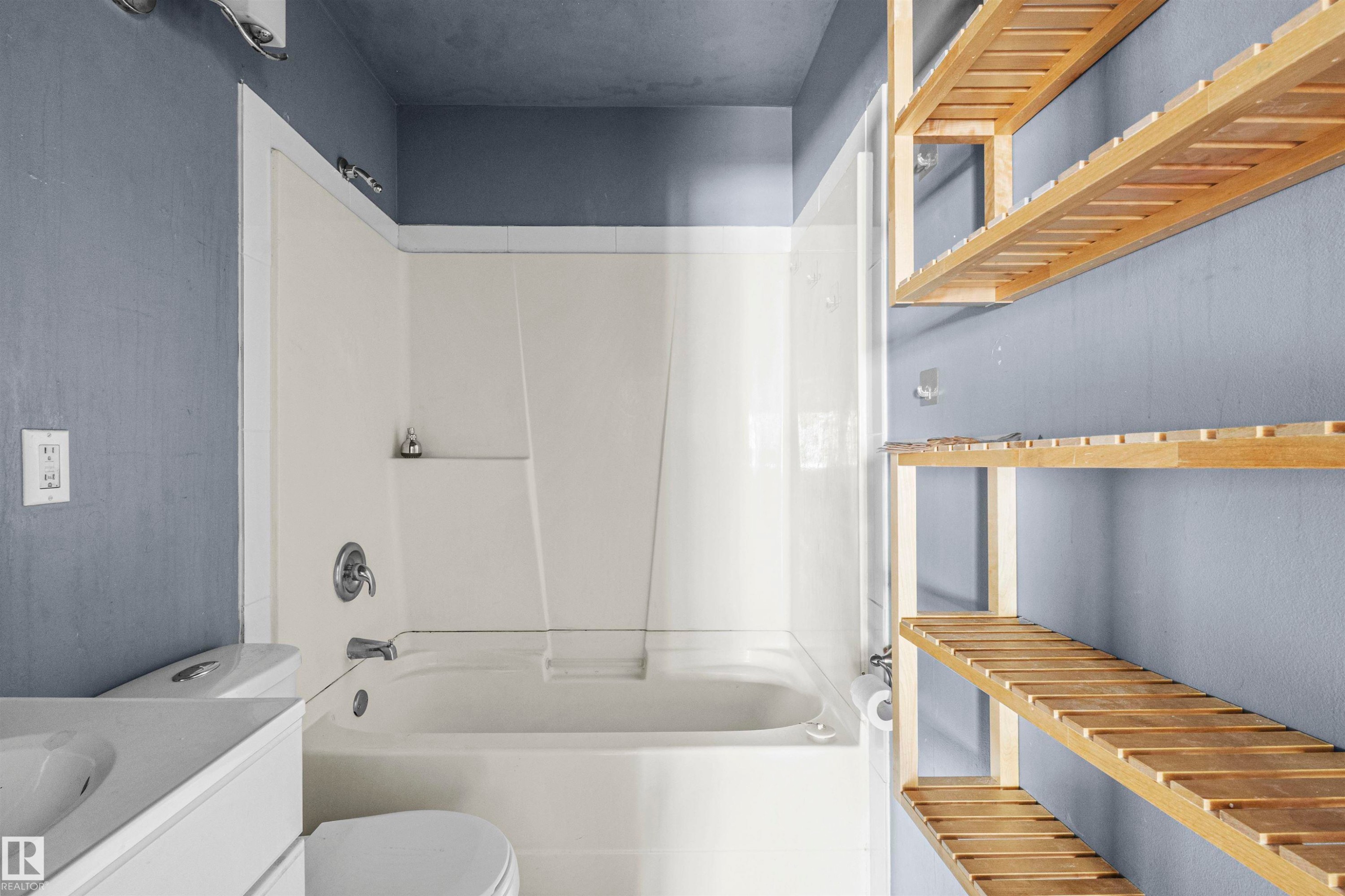 Bathroom featuring a white integrated tub and shower unit, chrome fixtures, a white toilet, and a white vanity with an integrated sink - 7520 106 Street, Edmonton, AB