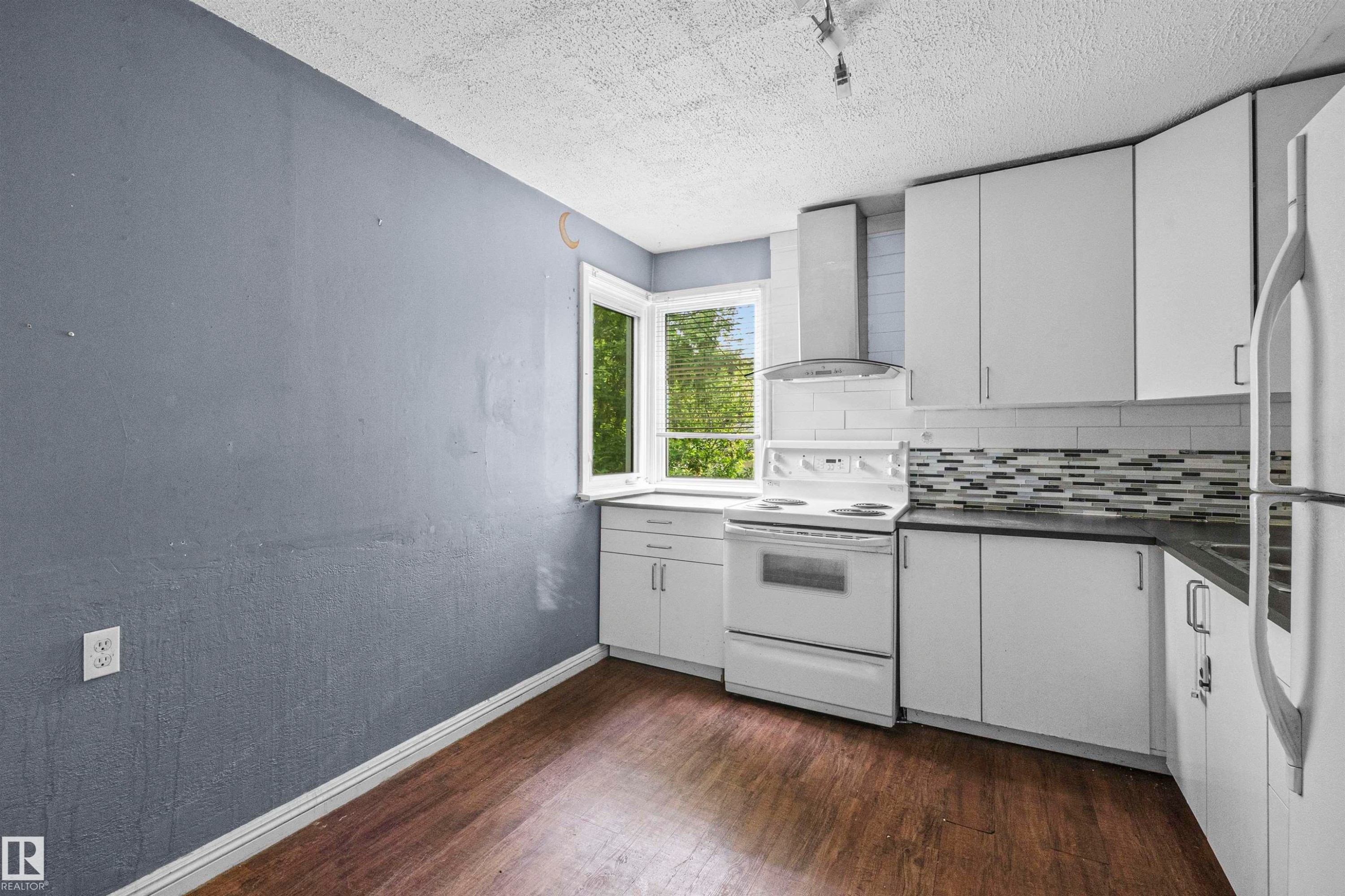 Kitchen featuring white cabinetry, dark countertops, wood-finish flooring, and a decorative tile backsplash - 7520 106 Street, Edmonton, AB