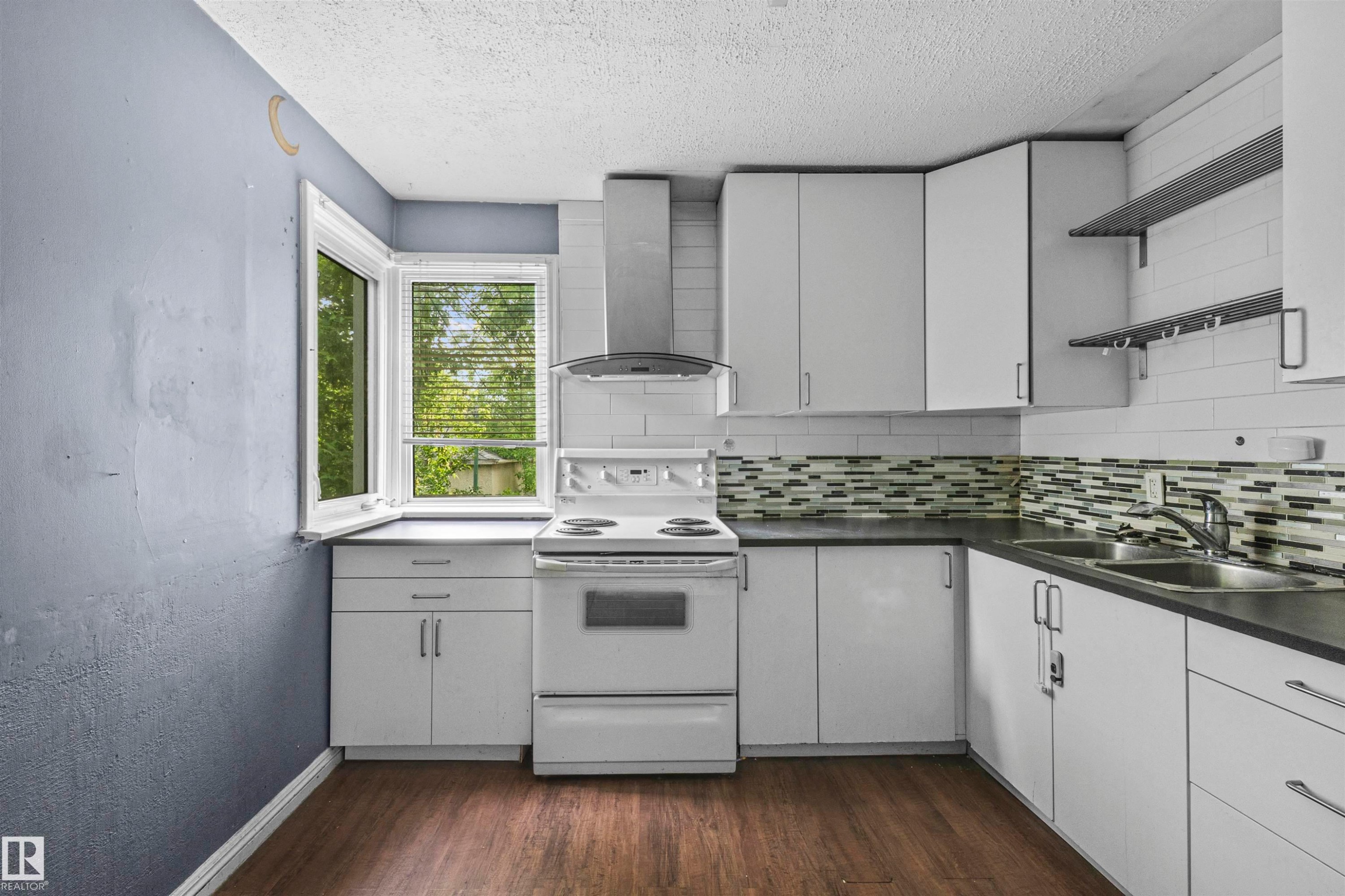 Kitchen featuring white cabinetry, dark countertops, a mosaic tile backsplash, a stainless steel range hood, and wood-finish flooring - 7520 106 Street, Edmonton, AB
