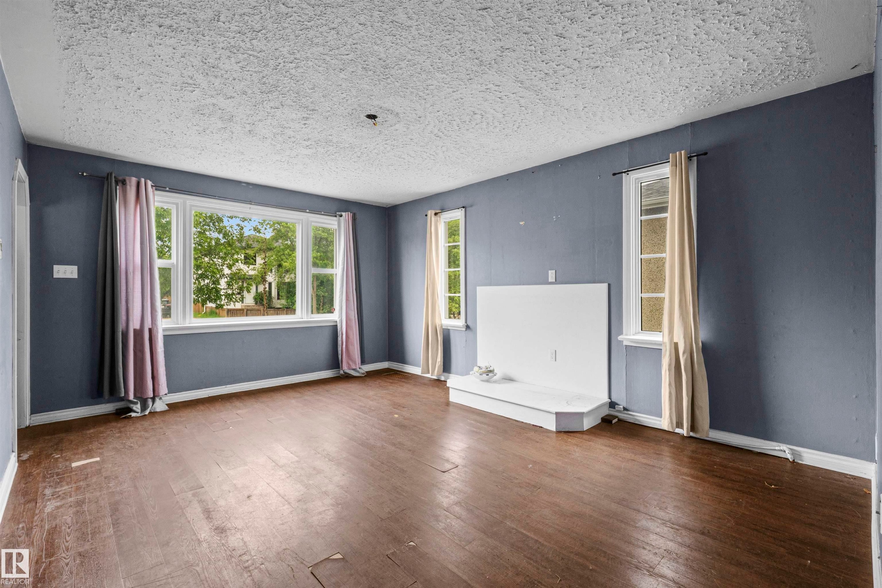 Spacious living area featuring wood-finish flooring, a prominent bay window, and a white built-in fireplace structure - 7520 106 Street, Edmonton, AB