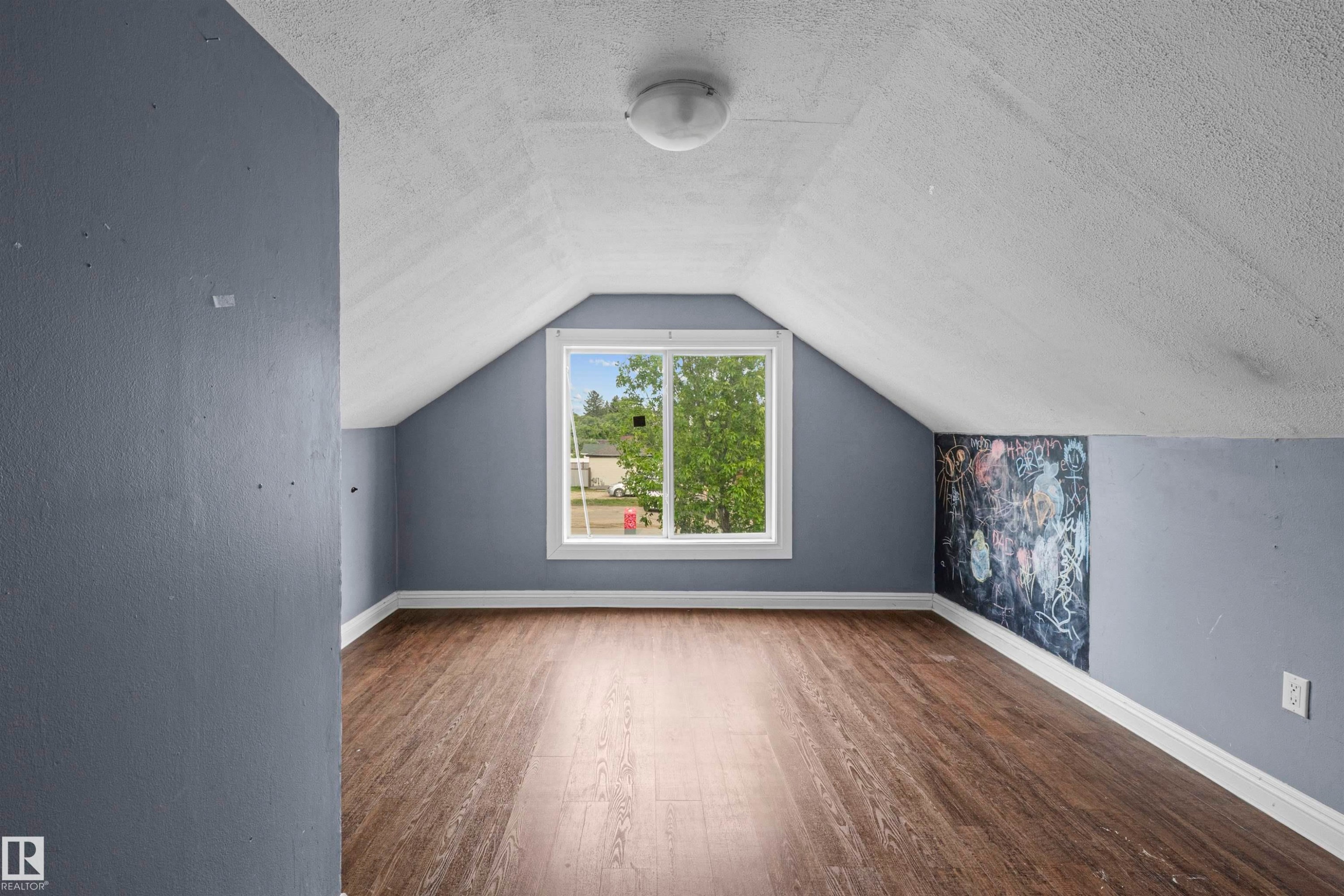 Room featuring wood-finish flooring, a white trim window, sloped ceilings, and a corner accent wall - 7520 106 Street, Edmonton, AB