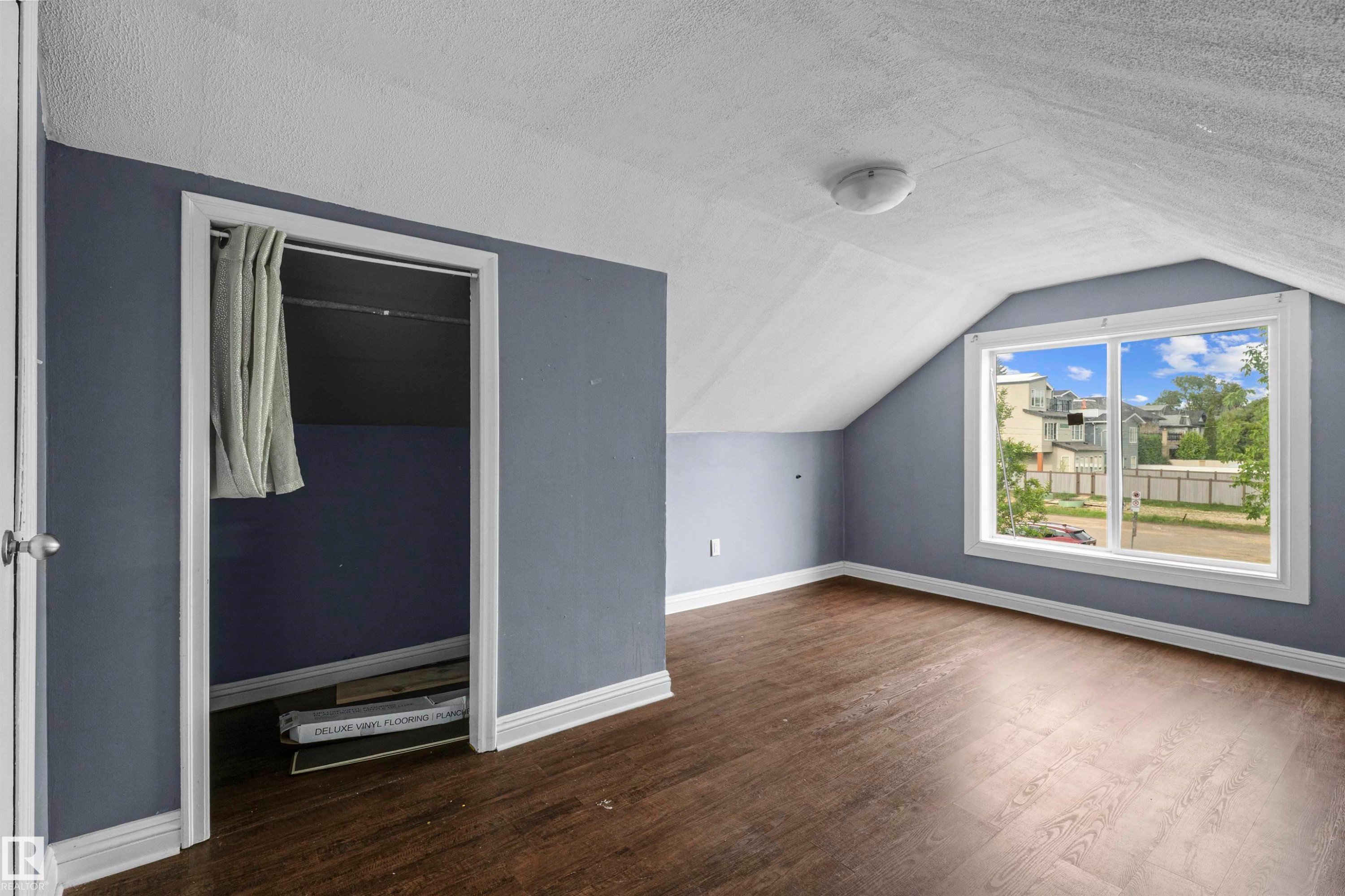 Attic space featuring wood-finish flooring, a large window with white trim, and sloped ceilings - 7520 106 Street, Edmonton, AB