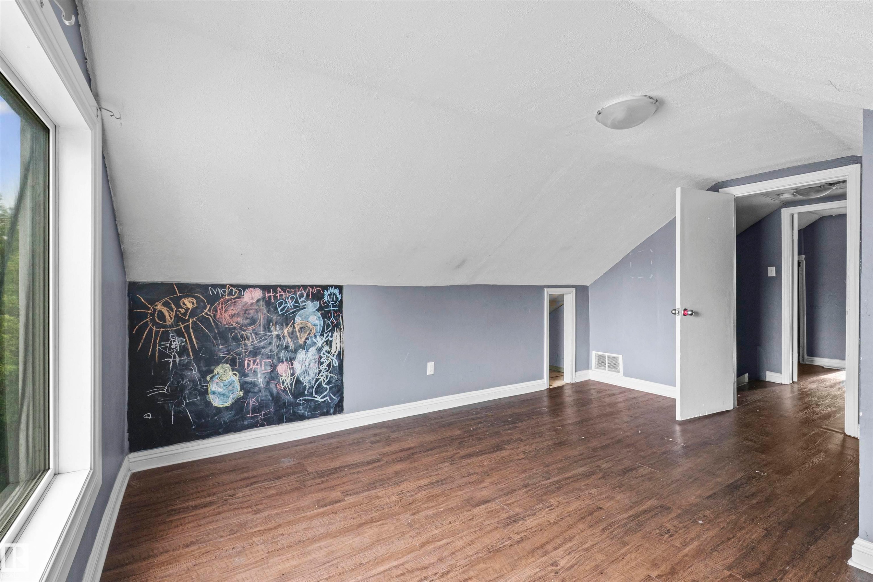 Attic room featuring wood-finish flooring, a large window, a built-in chalkboard wall, and recessed areas - 7520 106 Street, Edmonton, AB