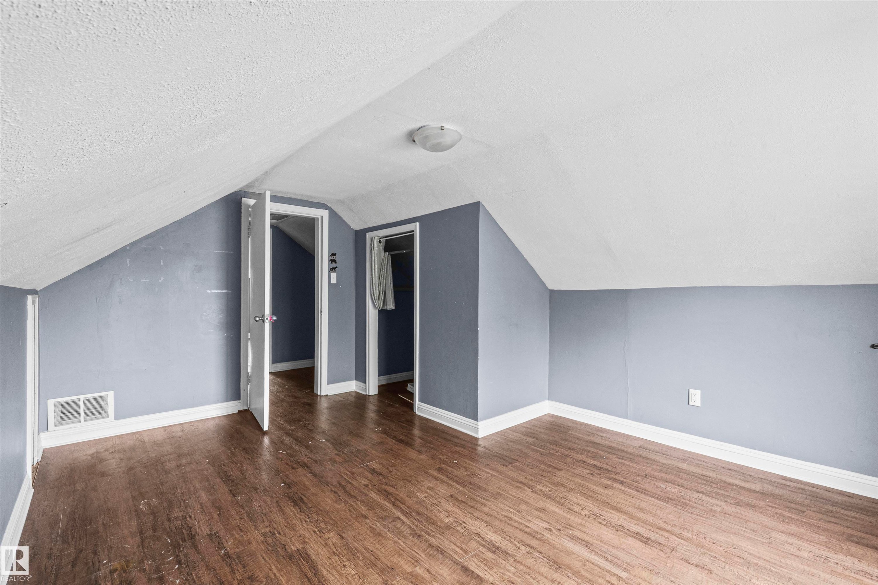 Room featuring wood-finish flooring, sloped ceilings, and light blue walls - 7520 106 Street, Edmonton, AB